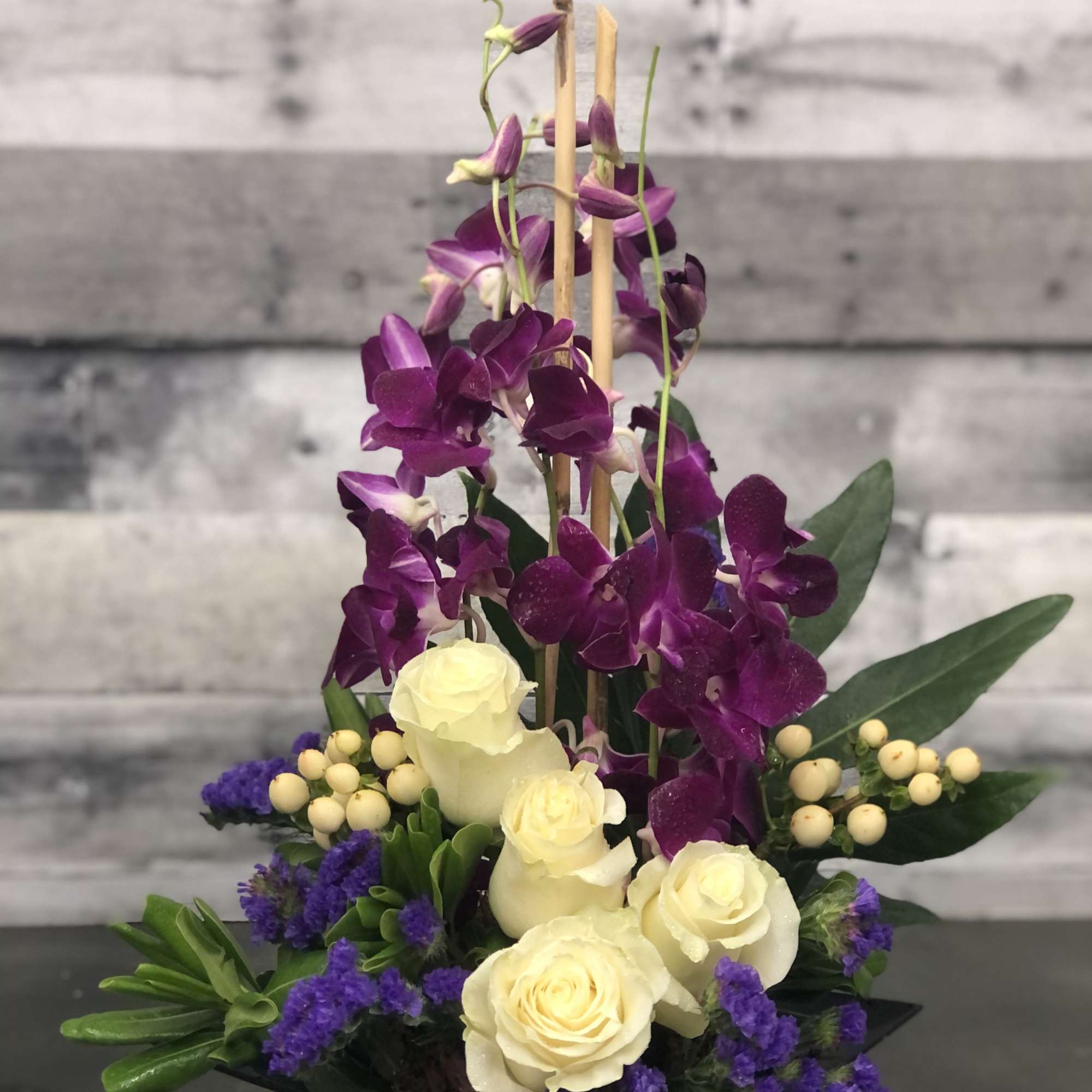 Dendrobium orchids, carnations, hypericum berries and statice dance around emerald leaves and