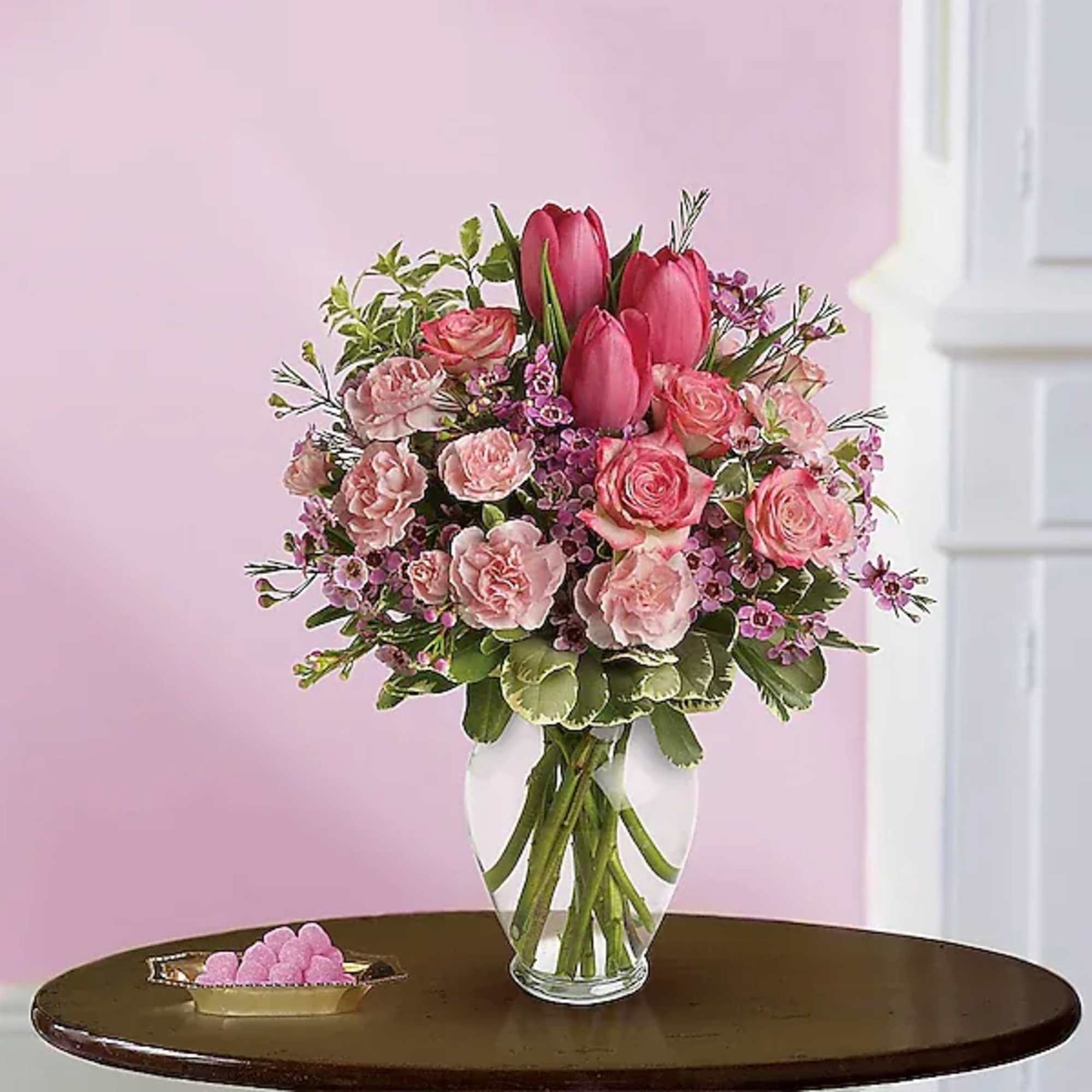 Spring into pink! Delicate roses, tulips and carnations fill a graceful vase