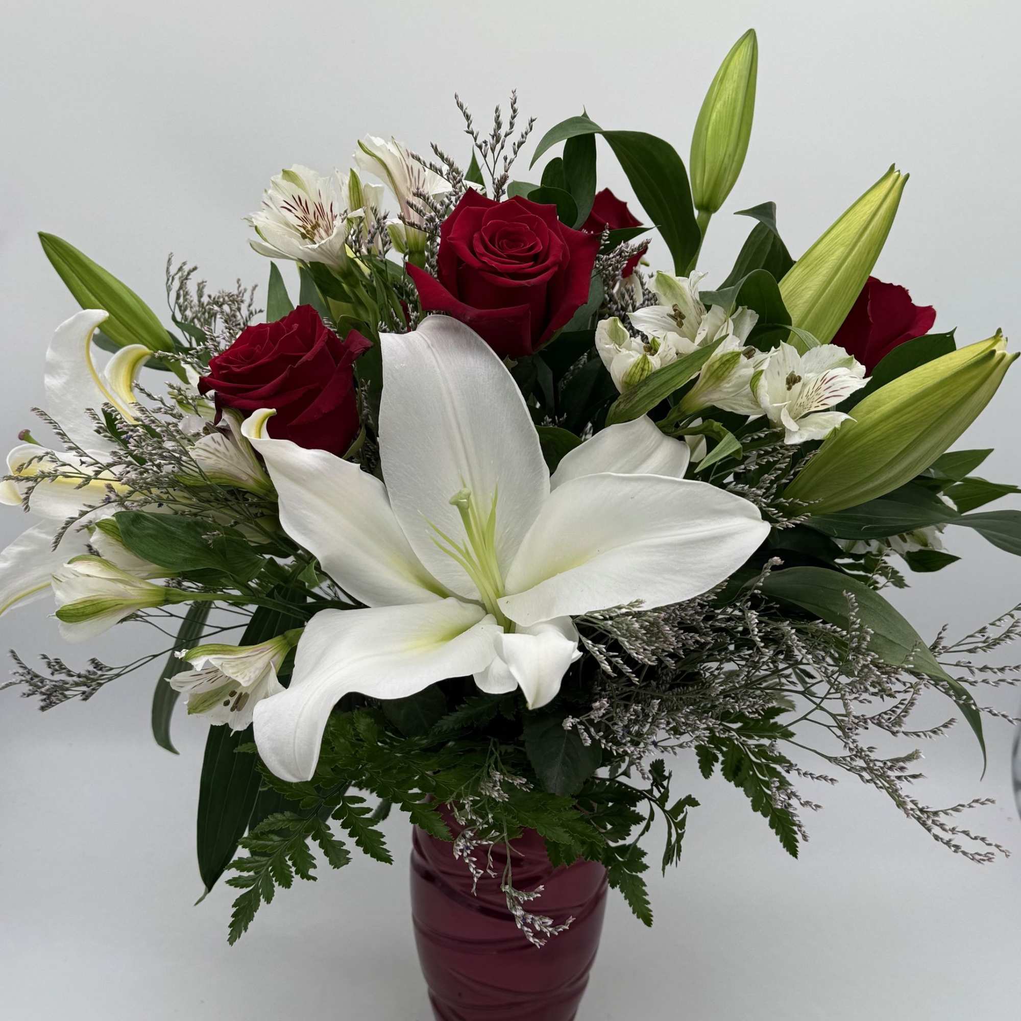Sweet, classic, and endlessly romantic, red roses with soft white lilies and
