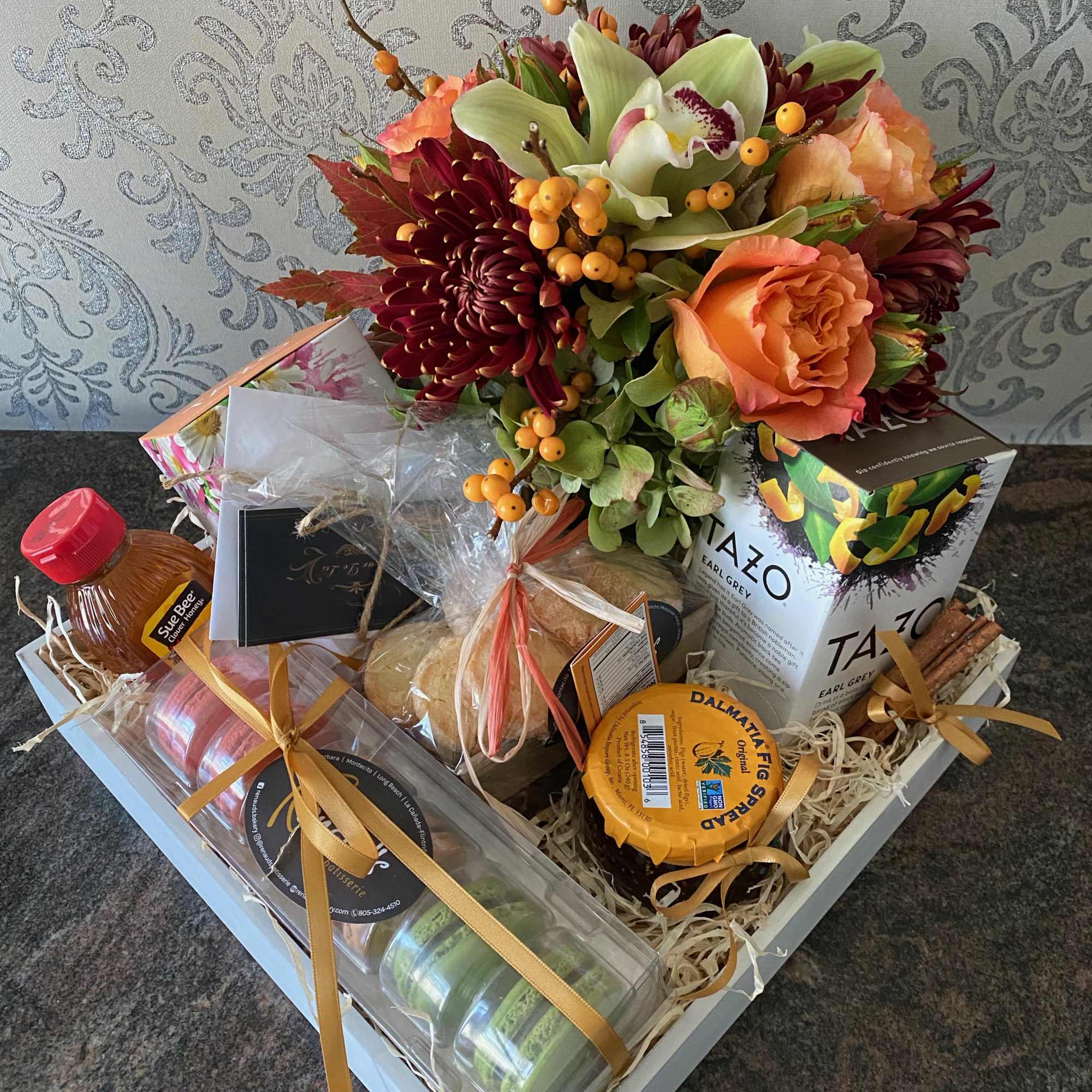 A box filled with assorted teas, cookies, honey and  seasonal arrangement