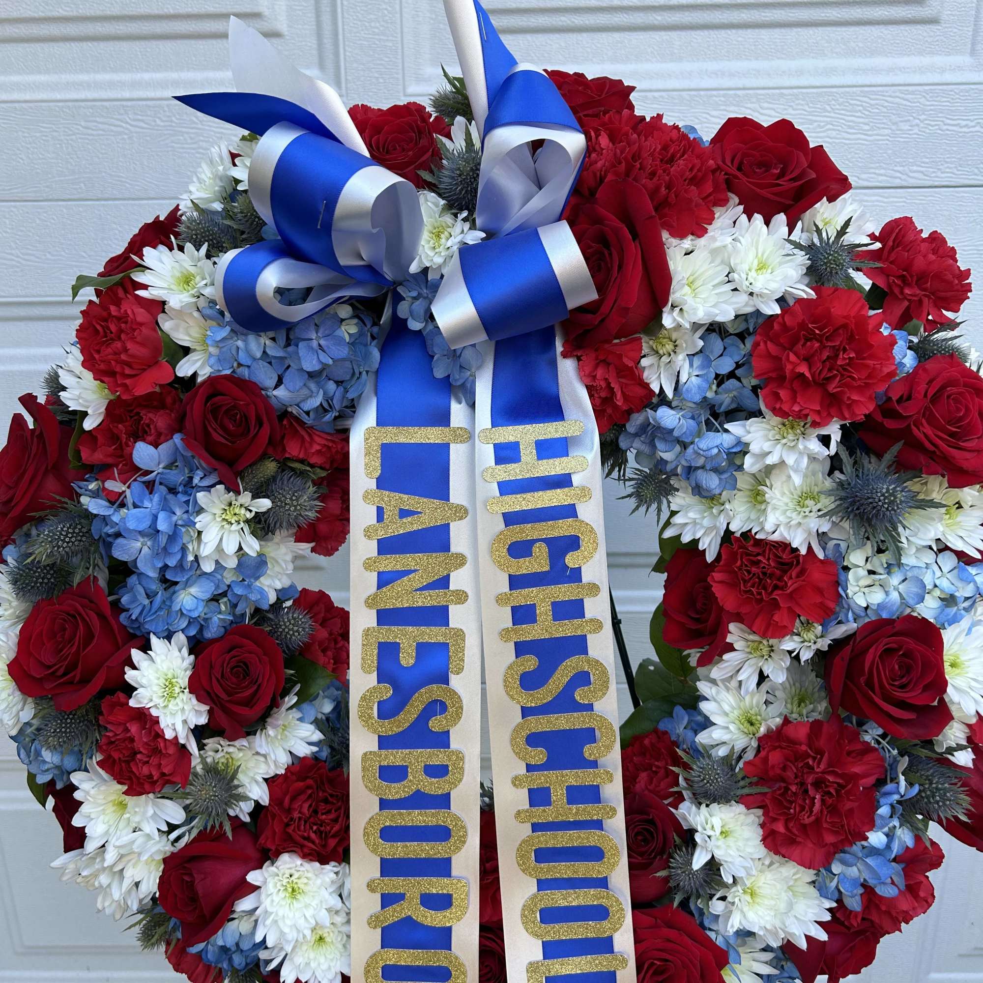 This red, white, and blue wreath includes roses, carnations, hydrangea, and mums
