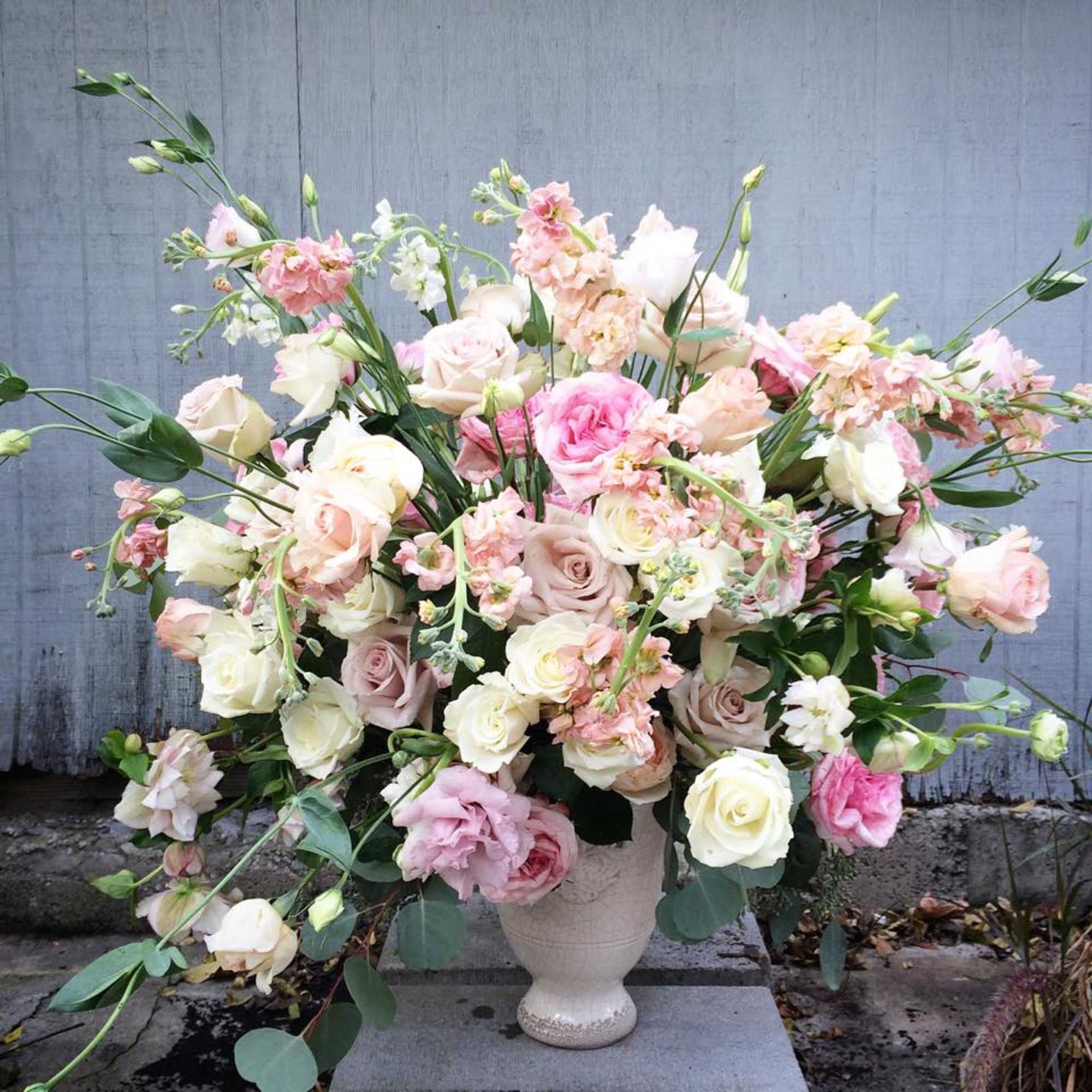 A grand, overflowing arrangement in soft pastels, featuring lush roses, delicate ranunculus