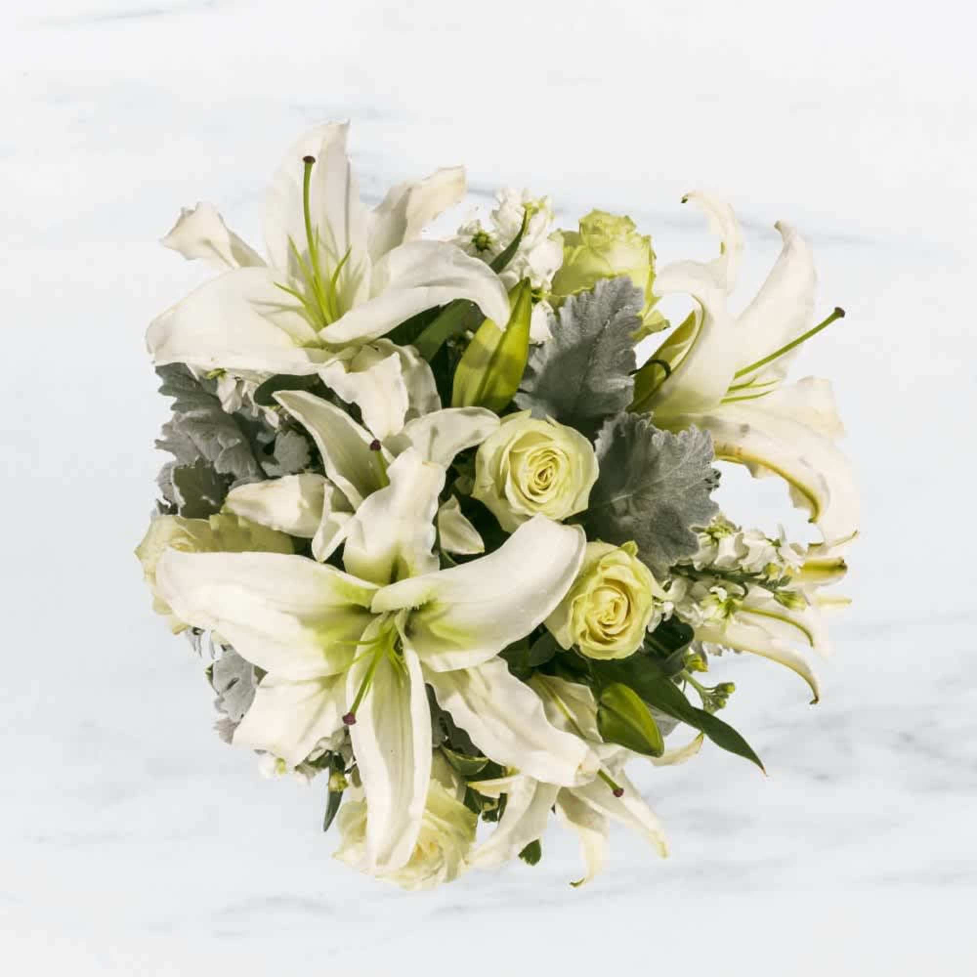 This arrangement includes white roses, white asiatic lilies, white stock, and dusty