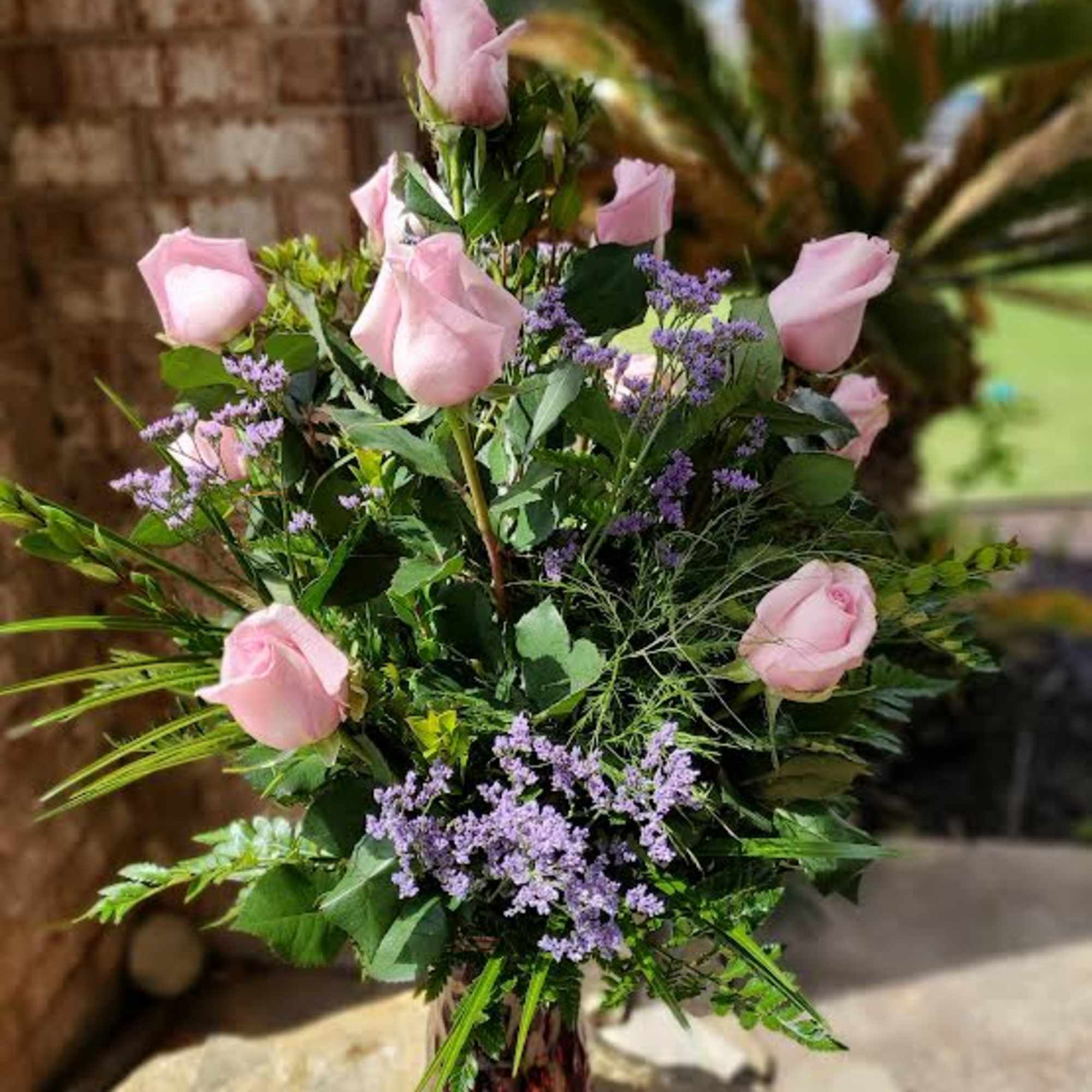 Twelve long-stemmed premium pink roses designed in a vase with complimenting lush