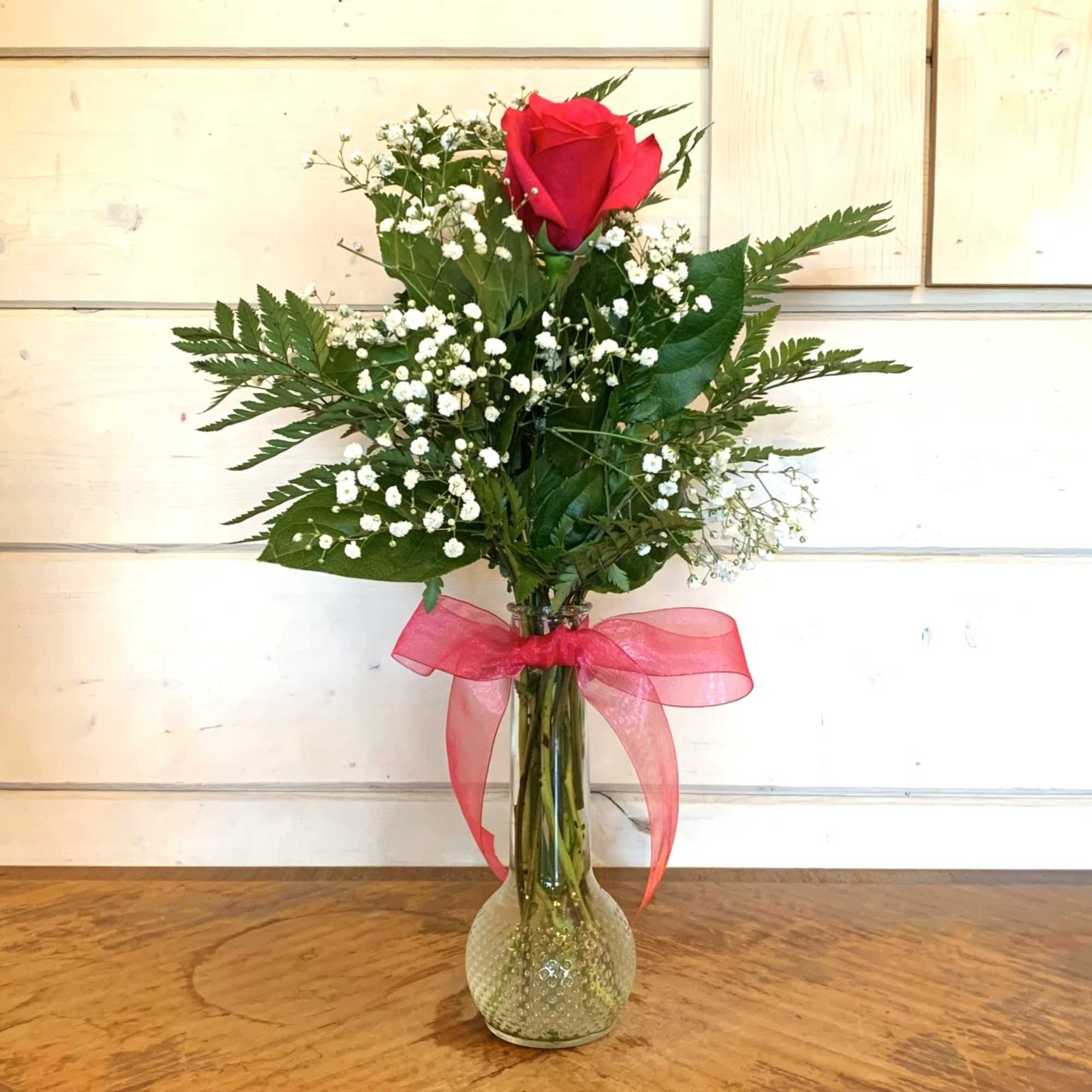 Hot pink rose, baby's breath and greens in a glass bud vase.