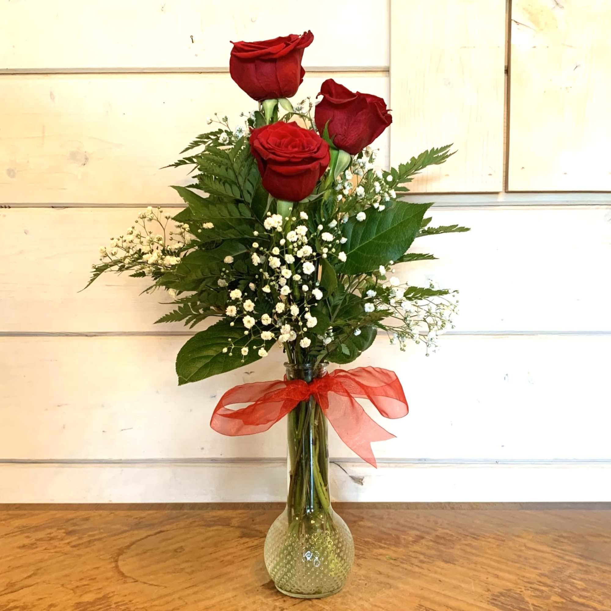 Red rose and baby's breath and greens in a glass bud vase.