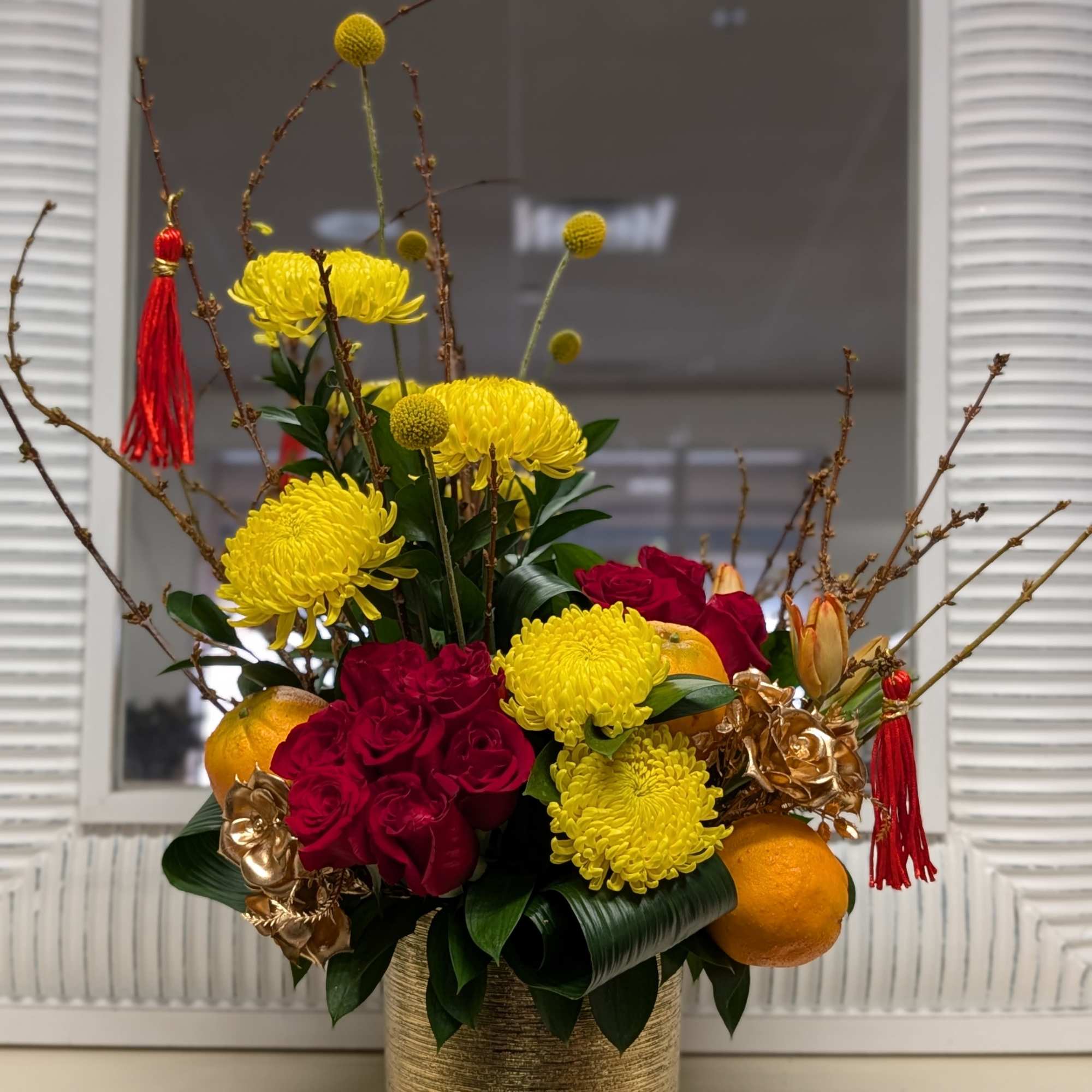 This beautiful arrangement of red roses, yellow chrysanthemum, faux oranges, blooming branch