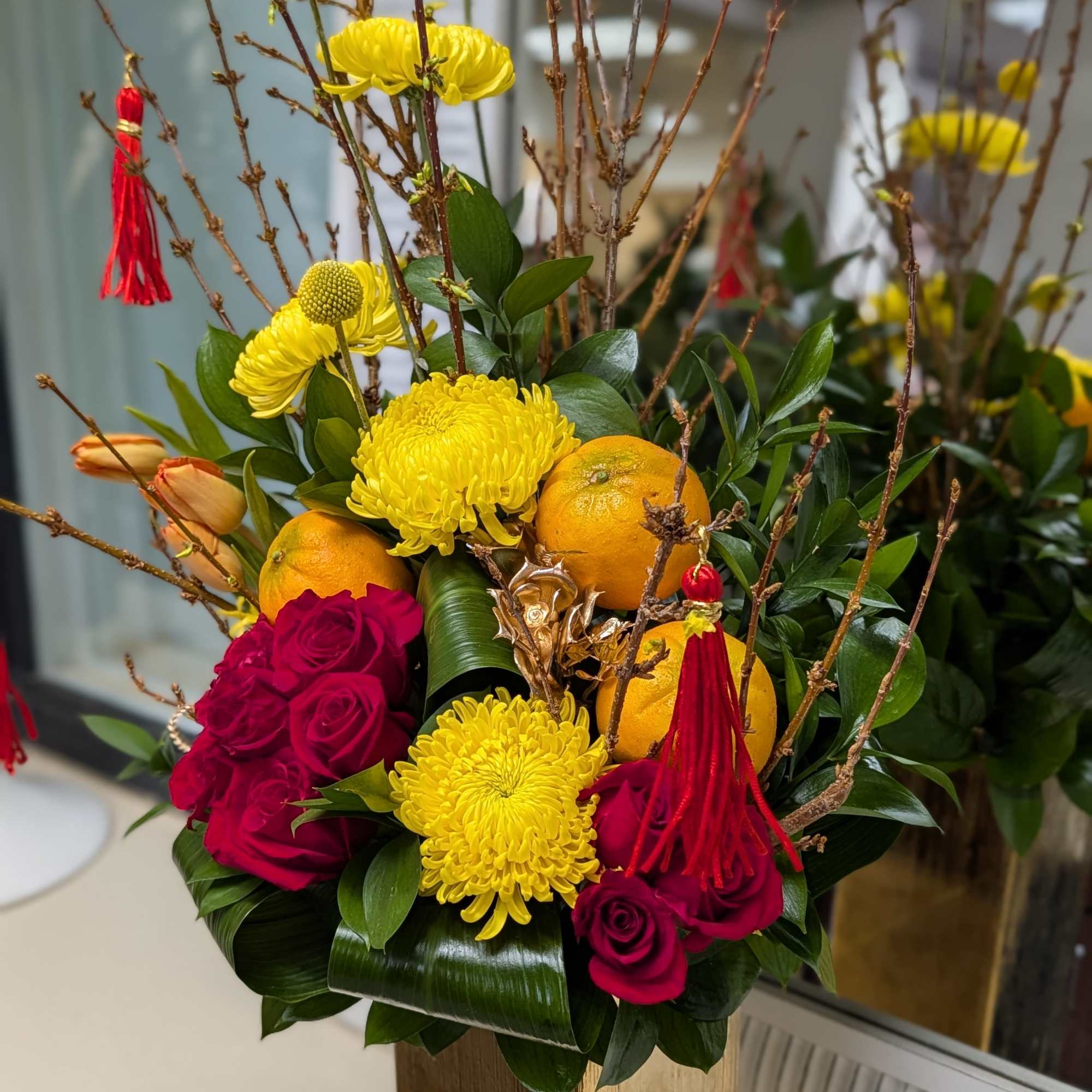 This beautiful arrangement of red roses, yellow chrysanthemum, faux oranges, blooming branch