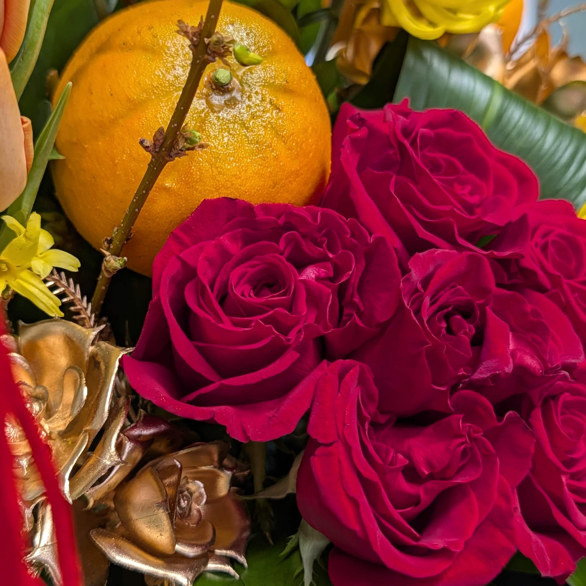 This beautiful arrangement of red roses, yellow chrysanthemum, faux oranges, blooming branch