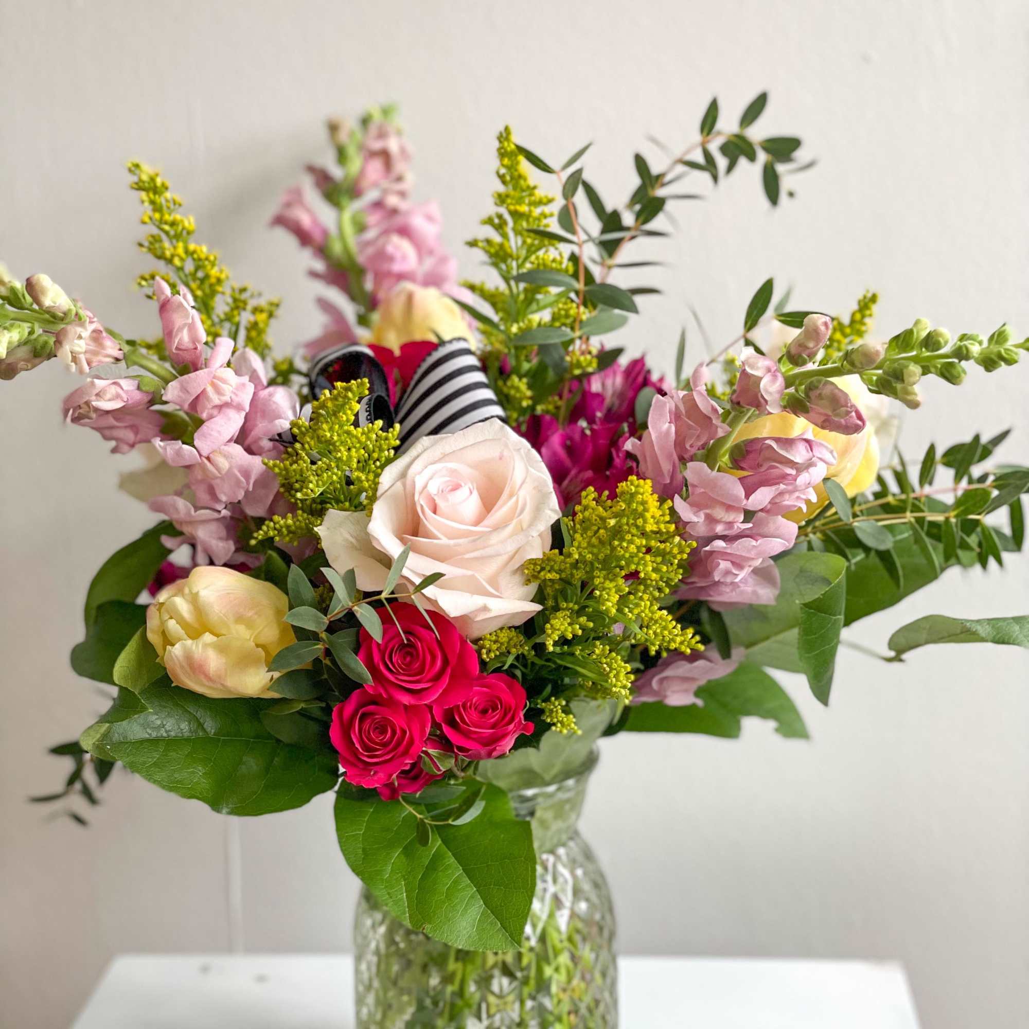 Sandy is a clear glass vase made up of snapdragons, roses, tulips