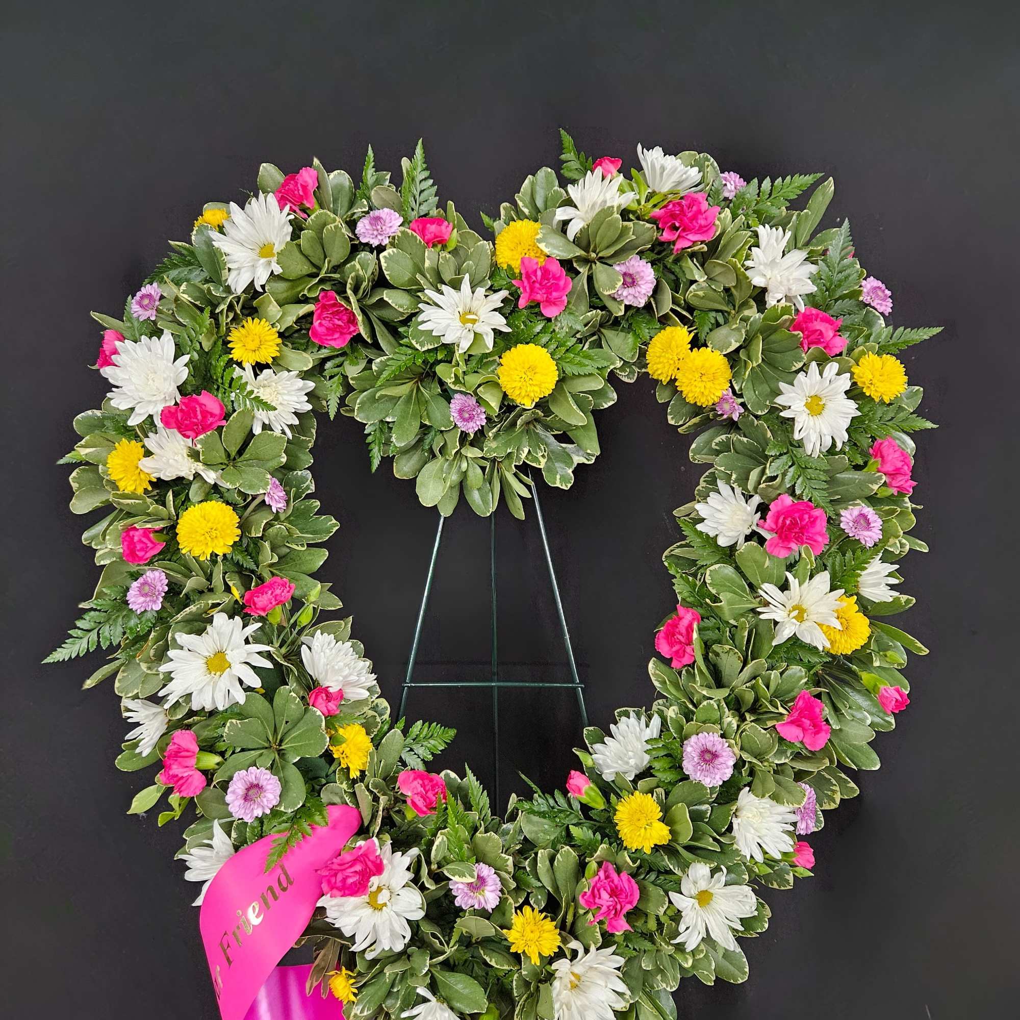 A heart shaped wreath ring covered in mixed flowers on a bed