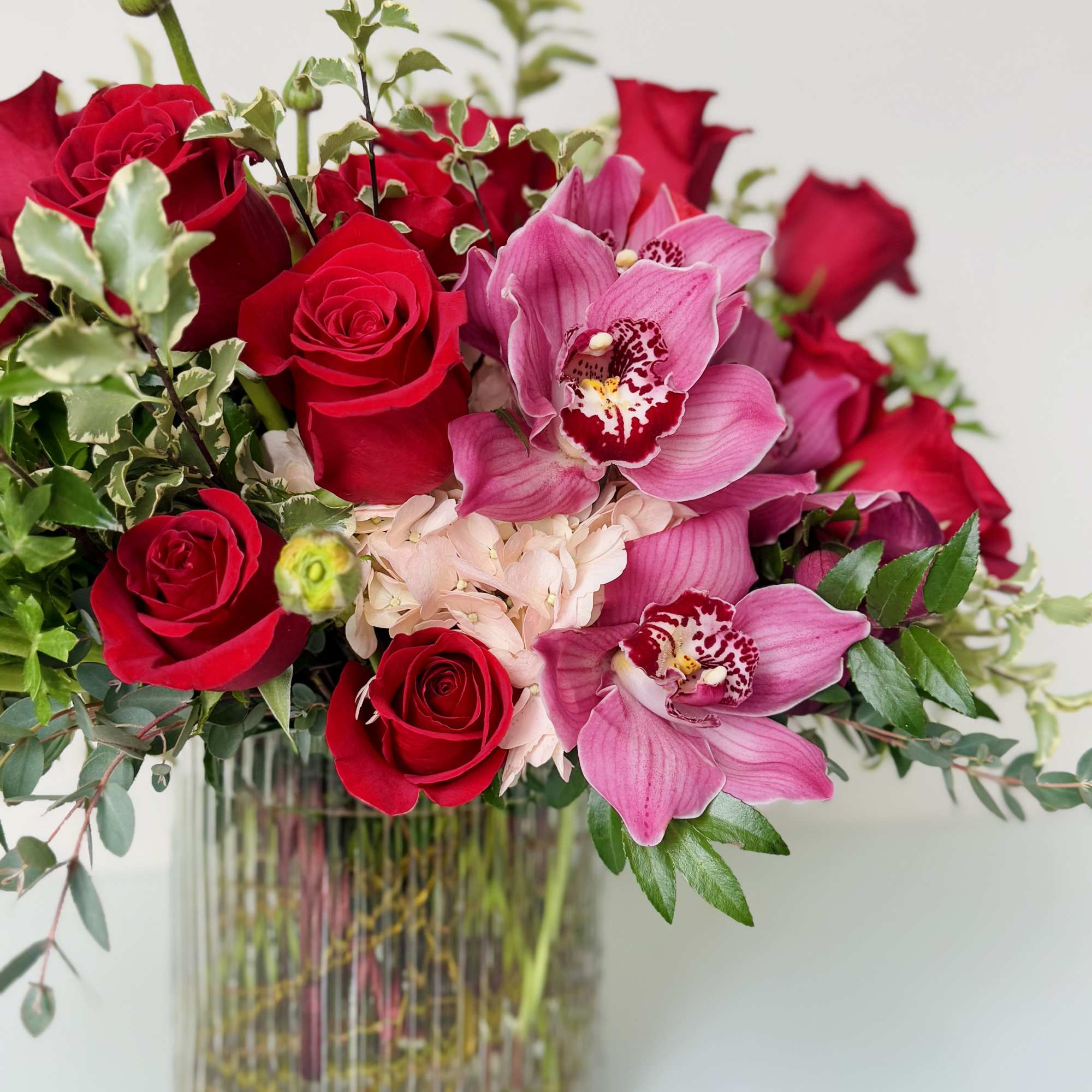 Beautiful one-sided flower arrangement with red mix blooms. Roses and cymbidium orchids