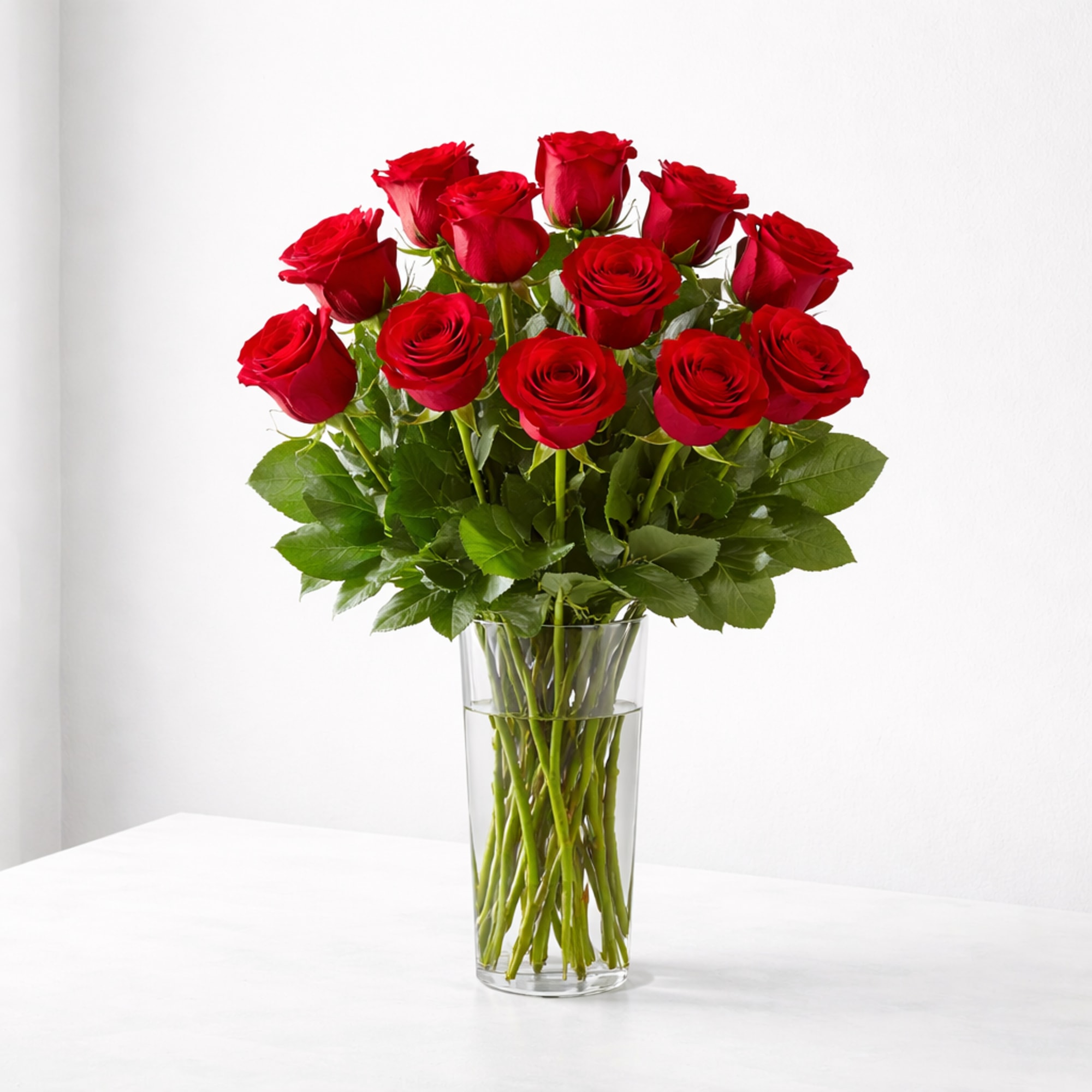 Classic long-stem red roses arranged in a sleek clear vase with greenery.