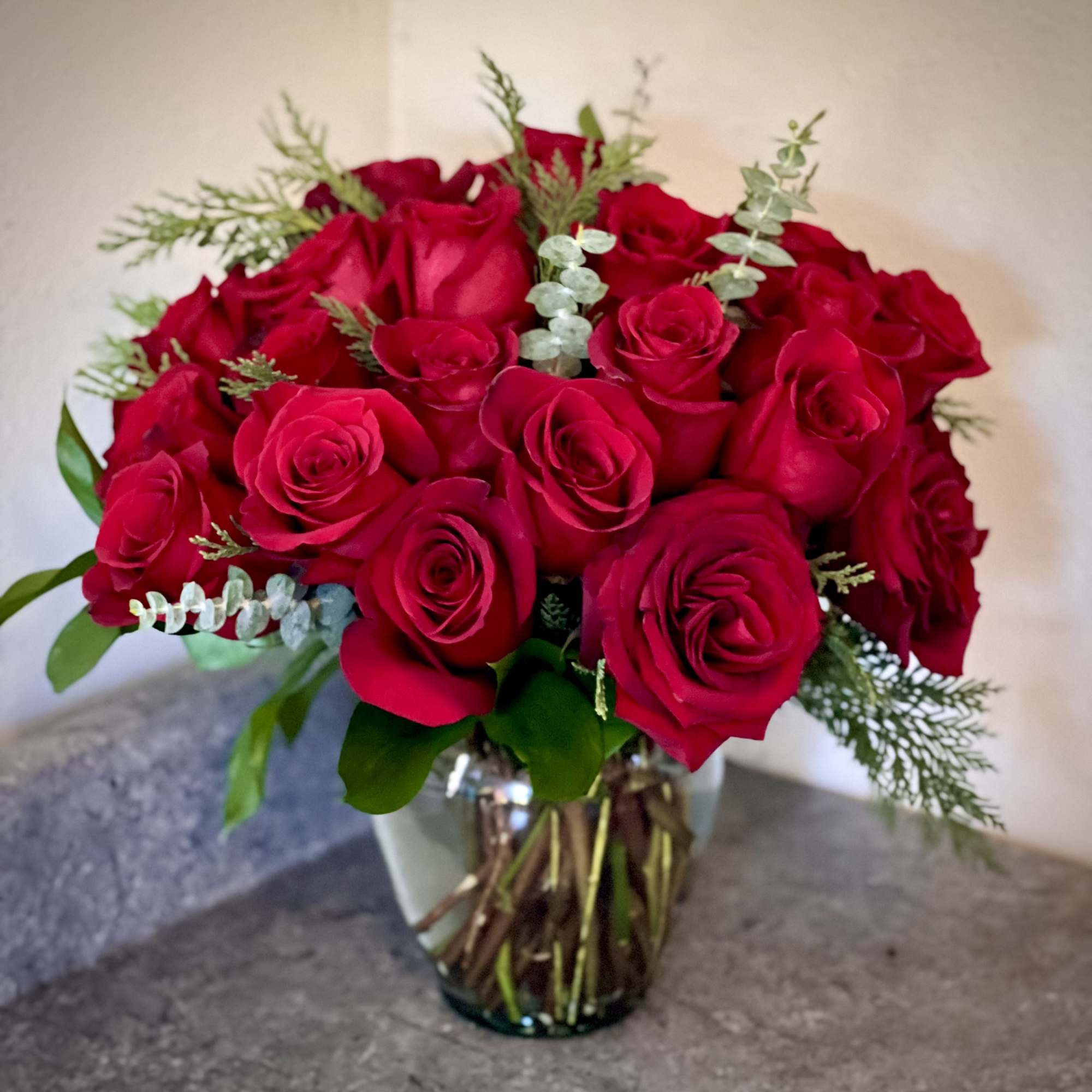 A dozen roses arranged with greenery and seasonal fill flowers in a