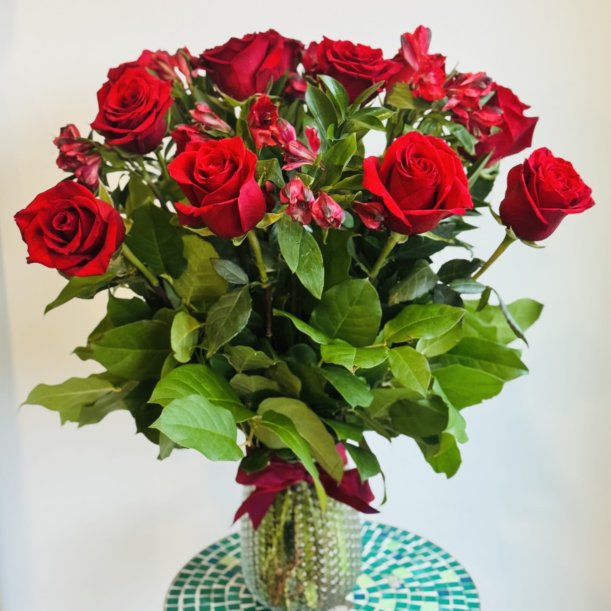 A dozen roses arranged with greenery and seasonal fill flowers in a