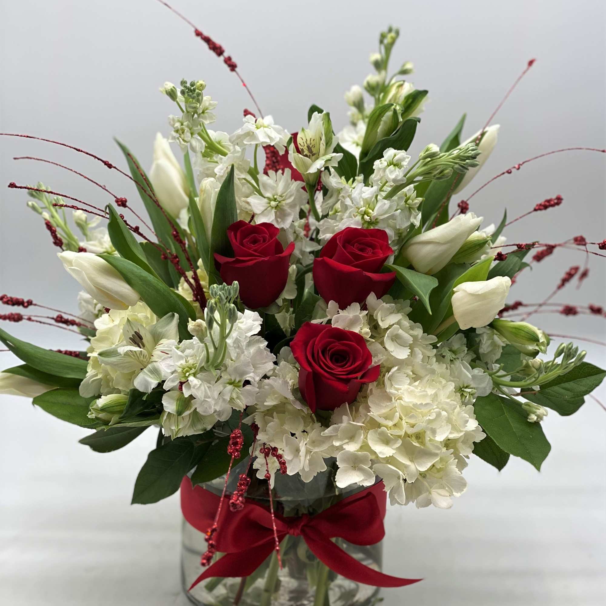 A lush mix of white and red blooms designed in a cylinder