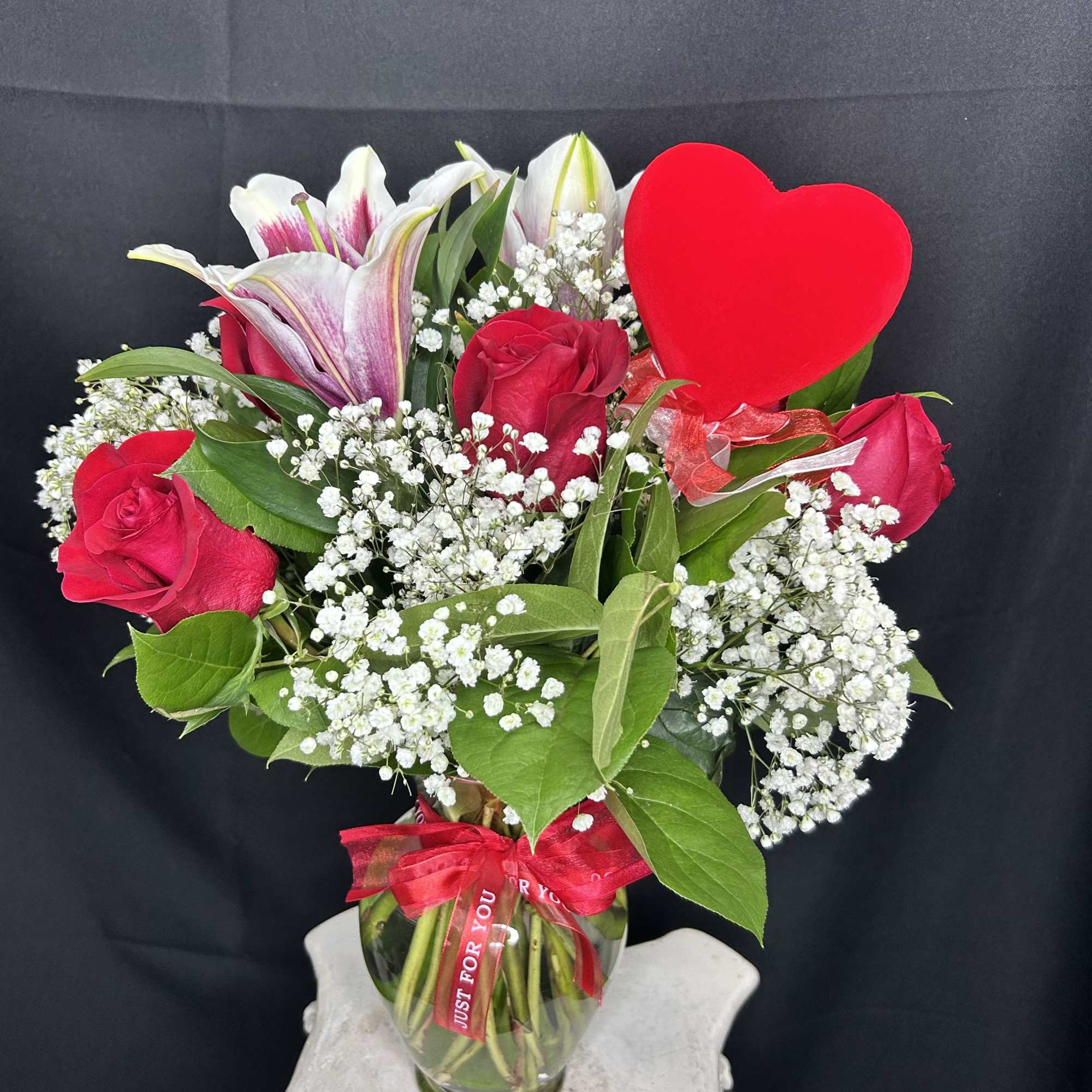 A medium-sized arrangement featuring 6 red roses, greenery, and baby's breath, accessorized