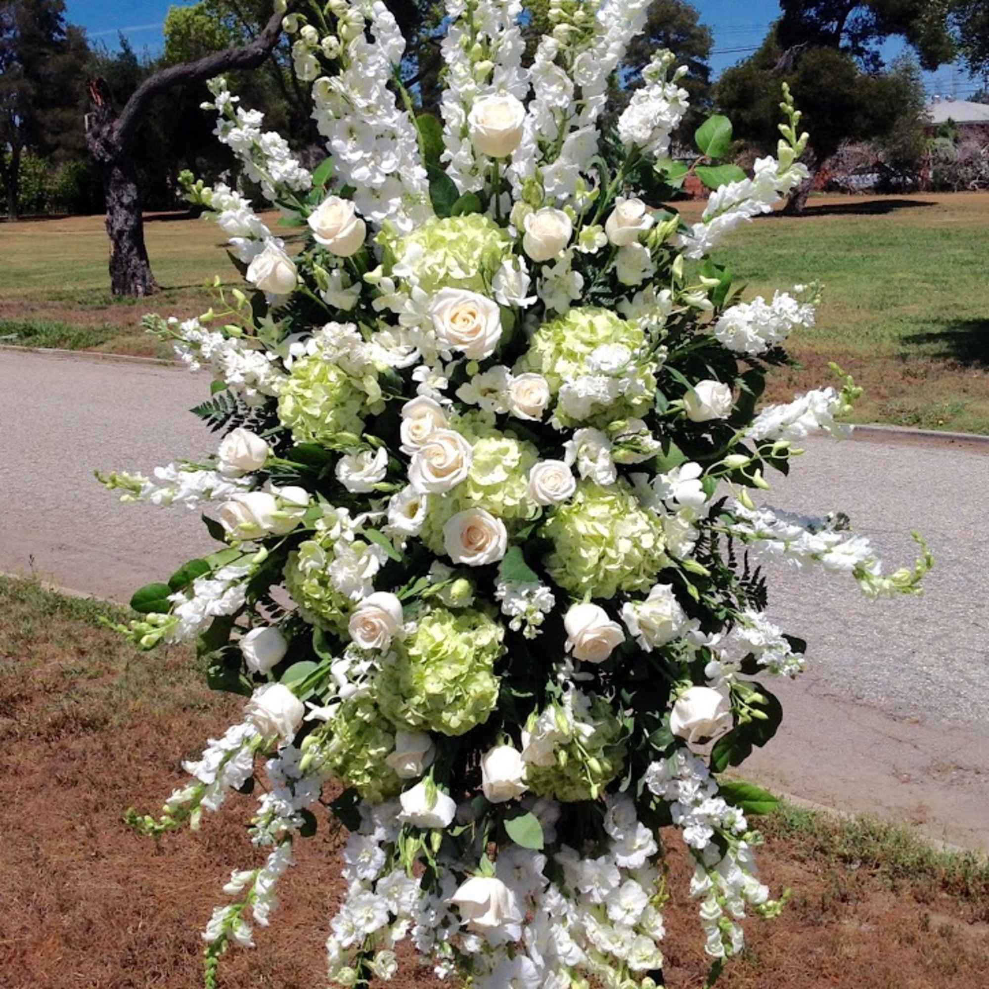 A traditional white and green standing spray with roses, hydrangea, and delphinium.
