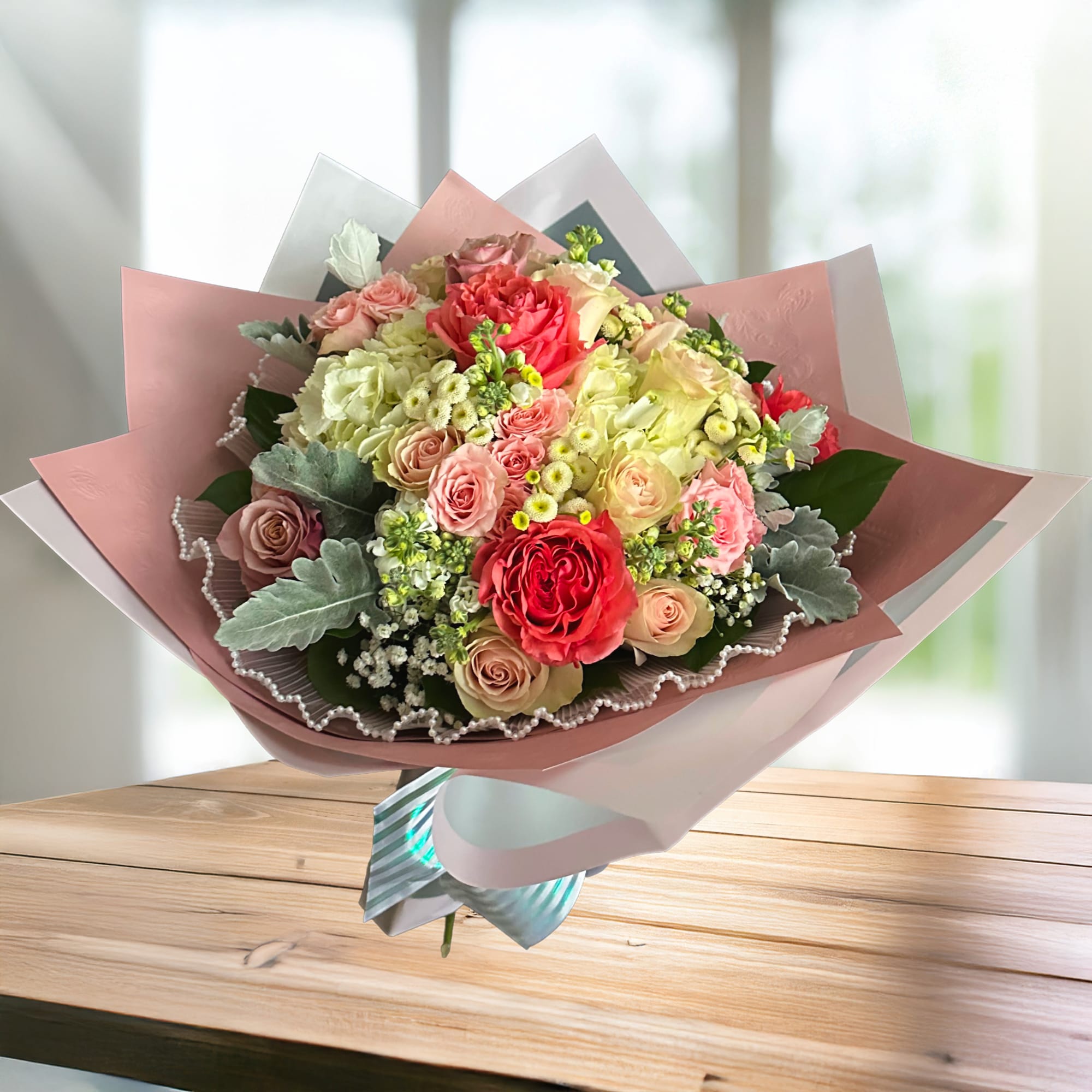 A romantic garden-style bouquet featuring blush and coral roses, creamy hydrangea, and