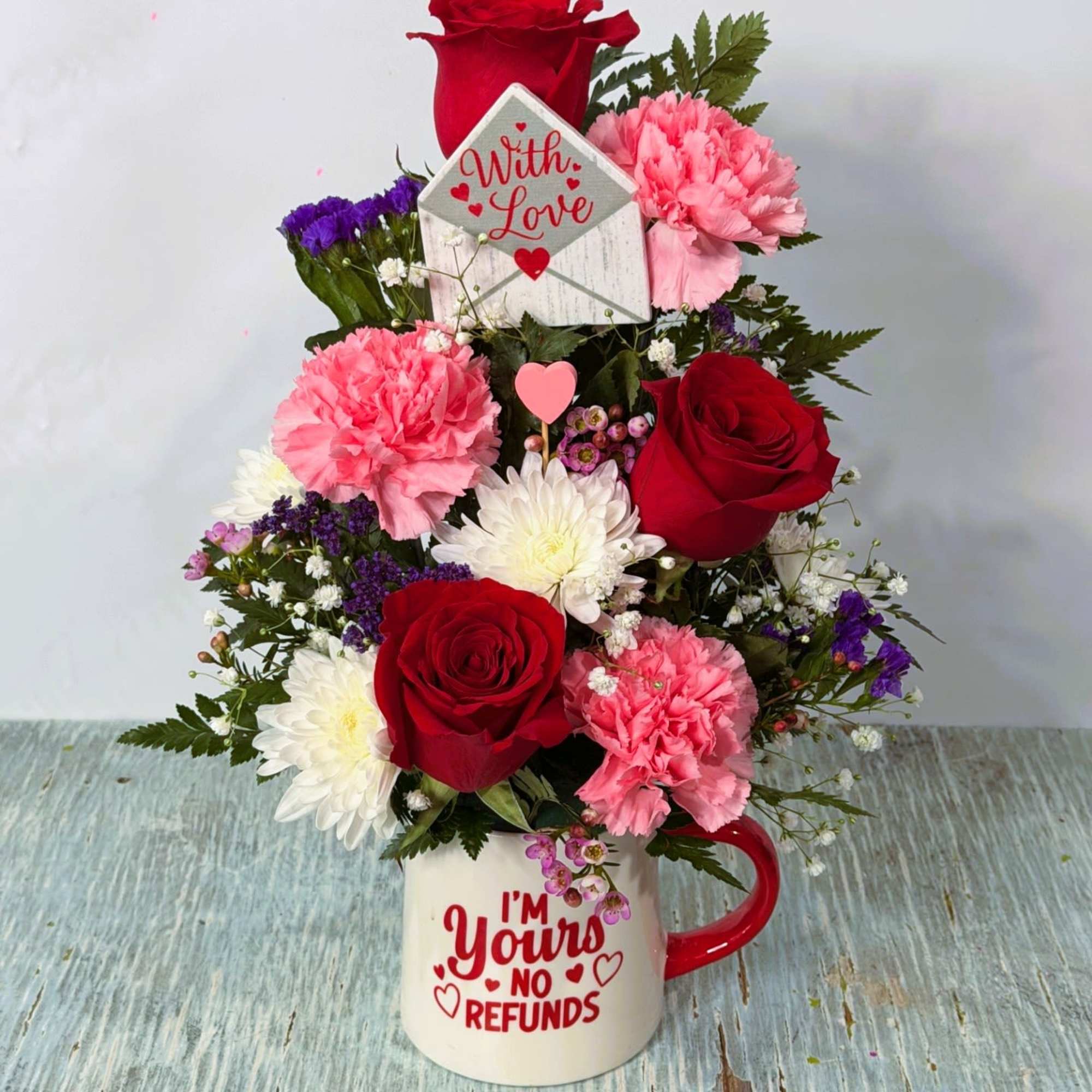 Arrangement of red roses, magenta carnations, lavender cushion poms, purple statice, babies