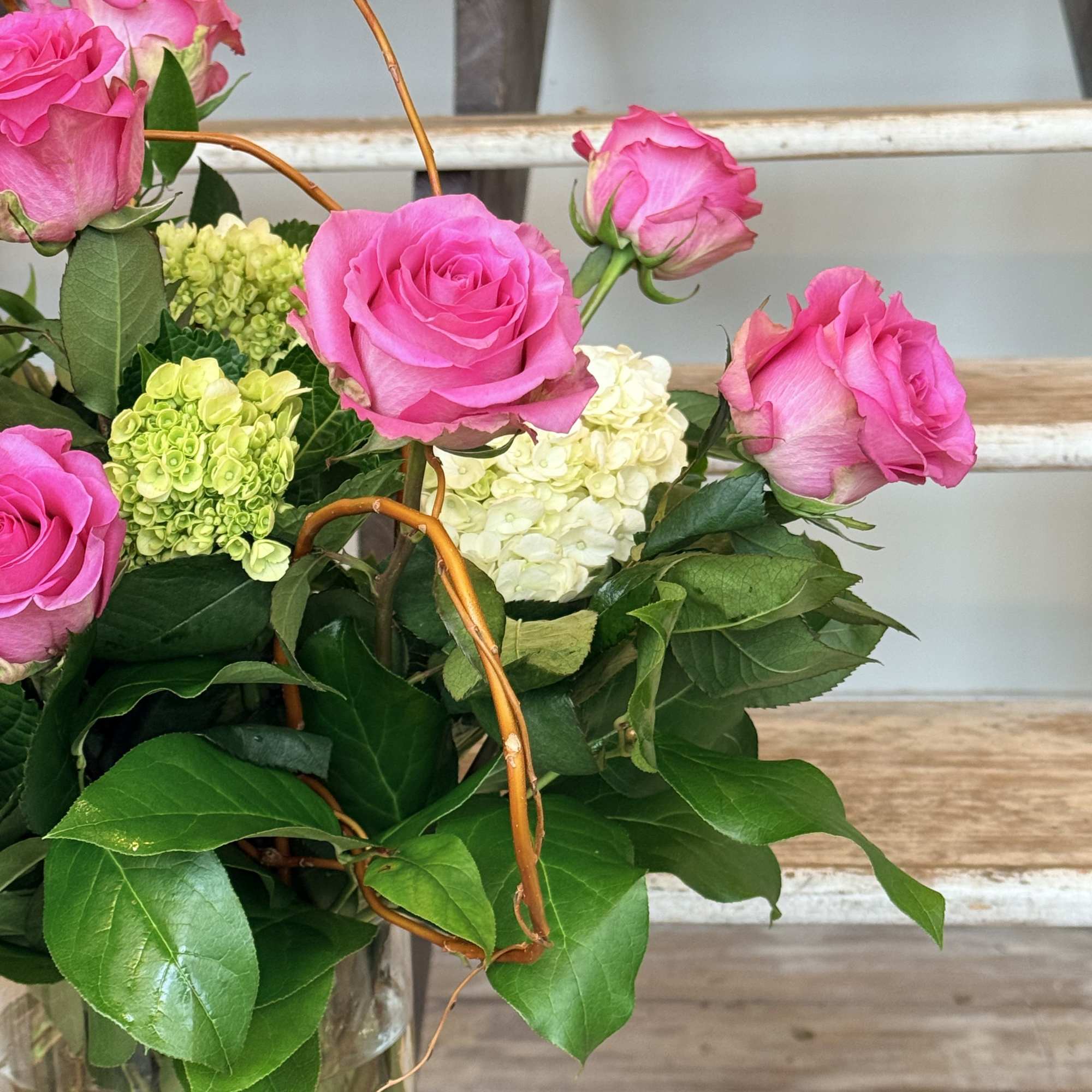 Pink Roses, green Mini Hydrangeas and lush greenery with curly willow accents.