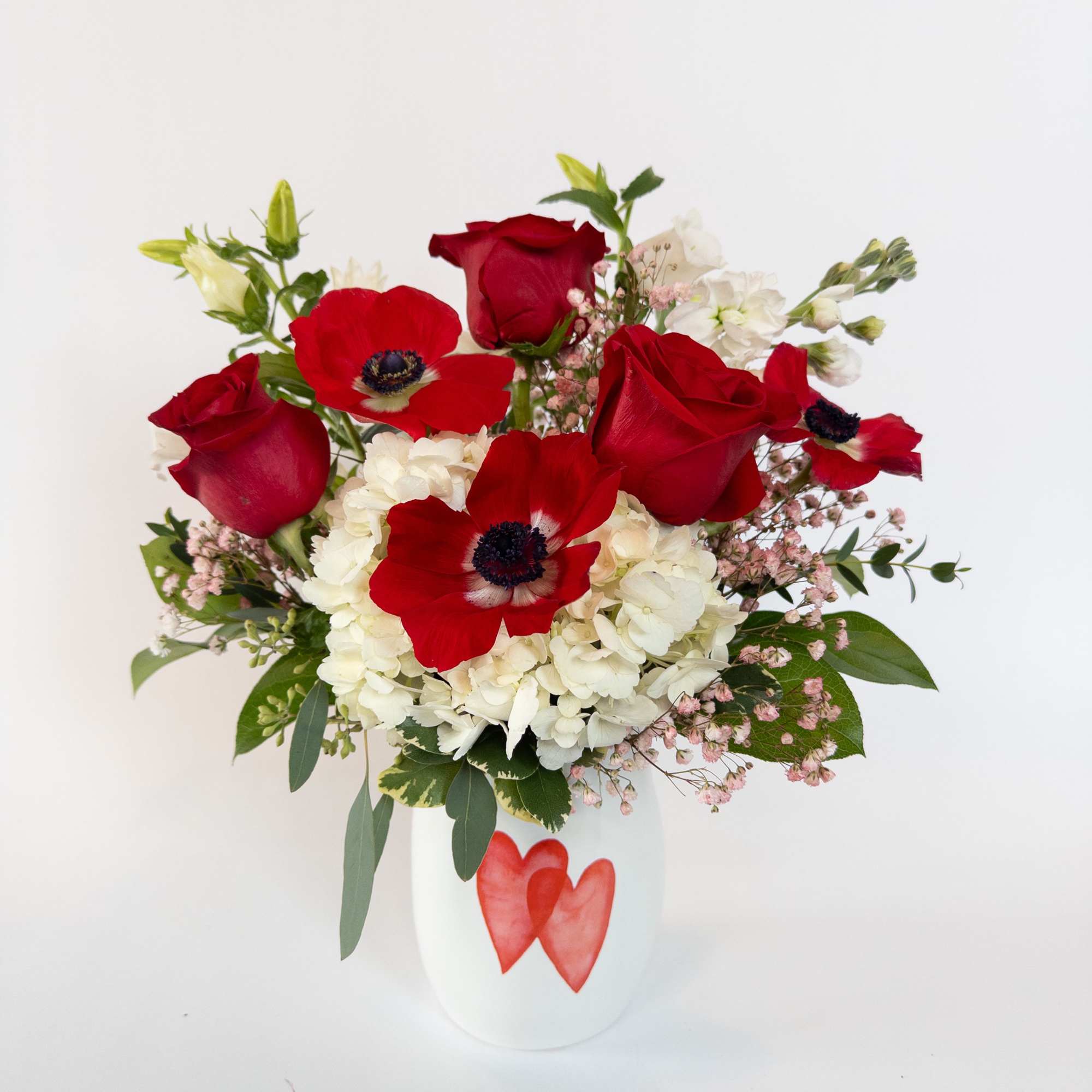 A white ceramic vase with 2 hearts on it filled with a