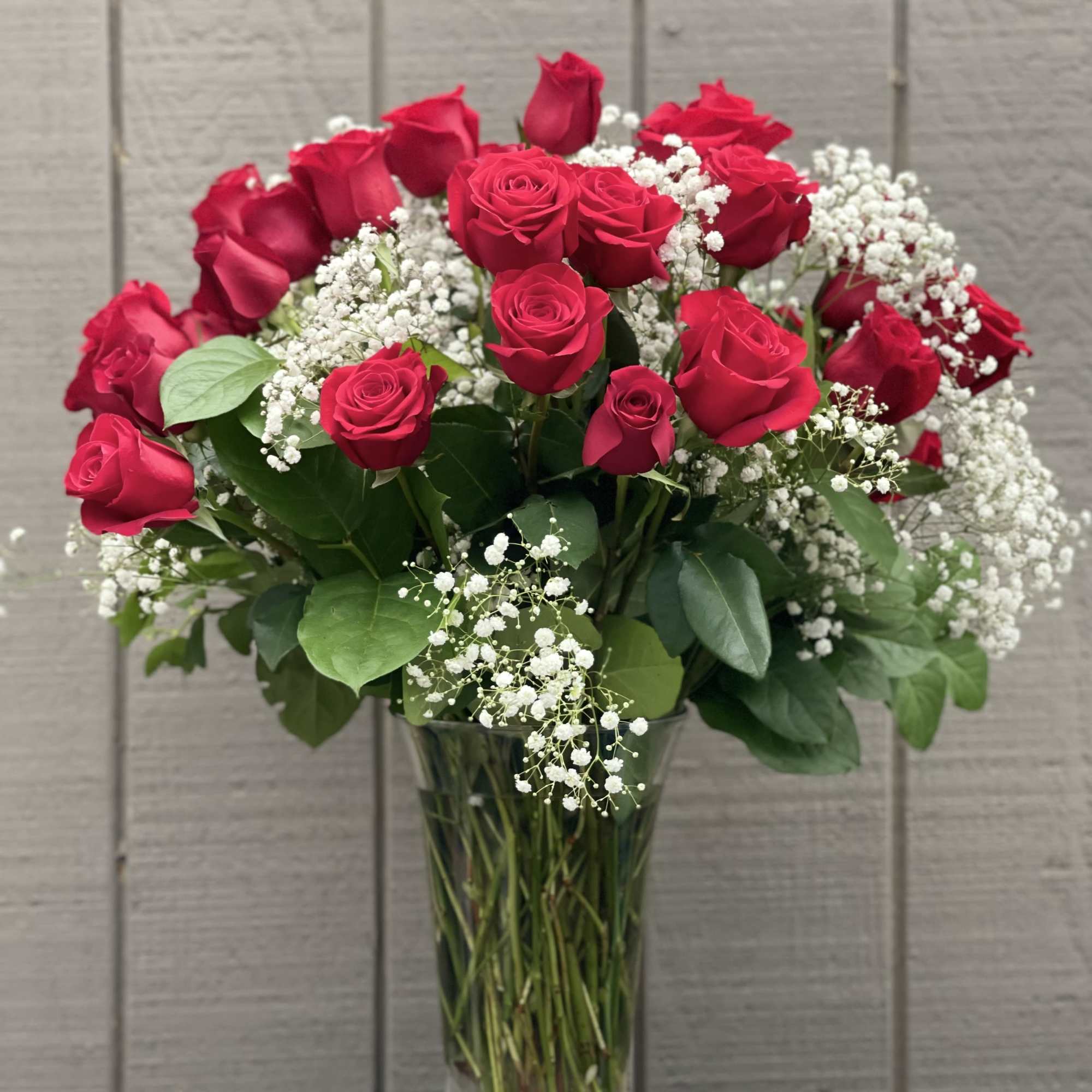 36 long stemmed red roses arranged in a vase with baby's breath