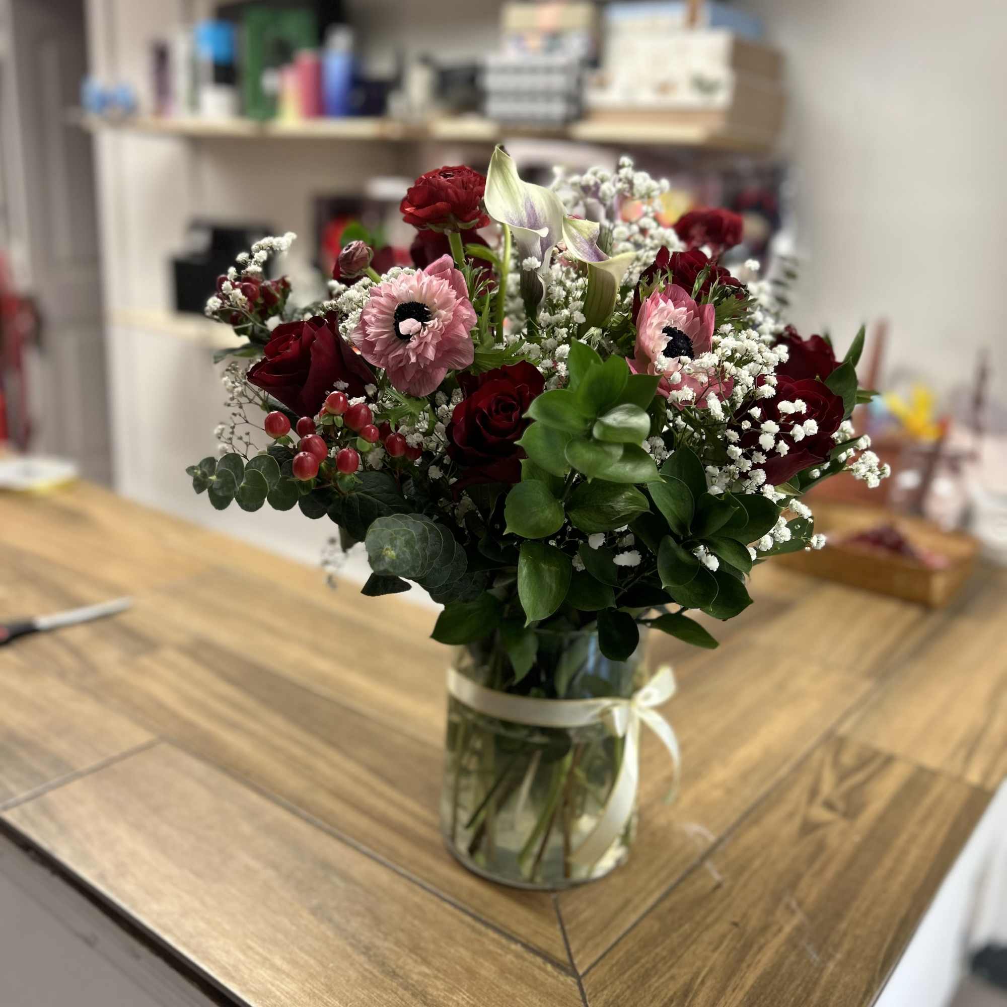 Assorted bouquet with red roses, ran&uacute;nculos, mini calla lilies, and green leaves.