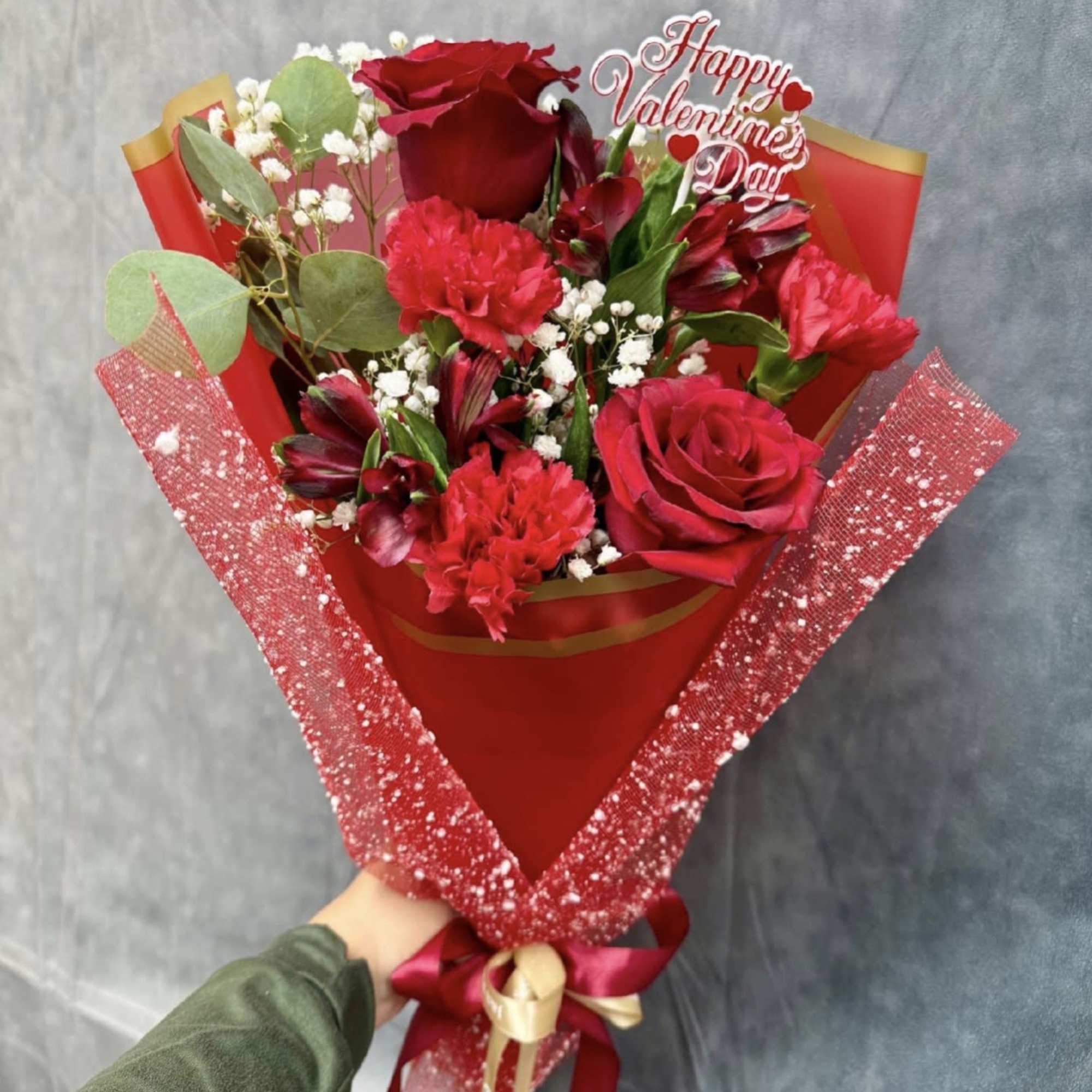 A romantic hand-tied bouquet featuring rich red roses, carnations, and alstroemeria, delicately