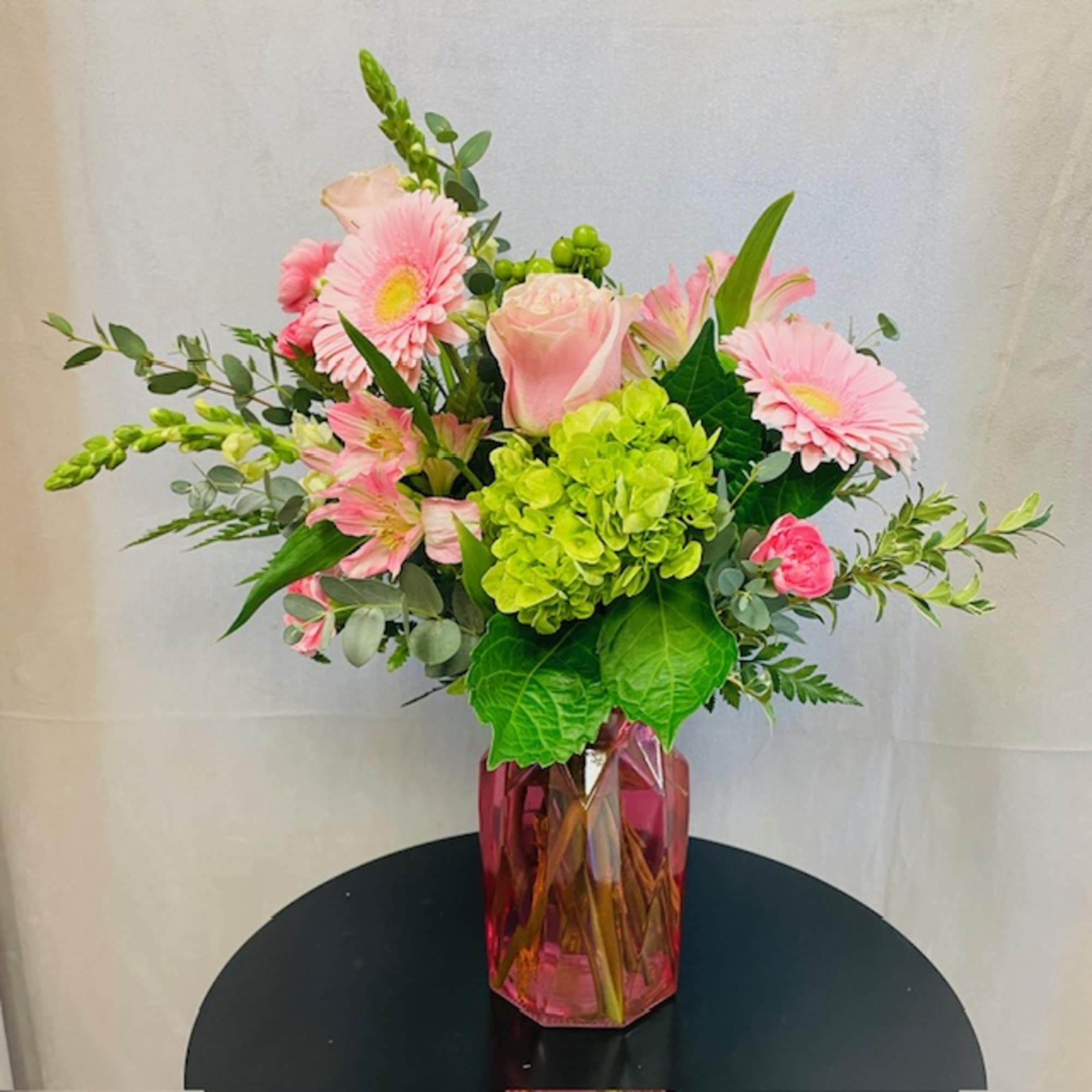 A vase arrangement with assorted flowers in soft pastel colors. Photos are
