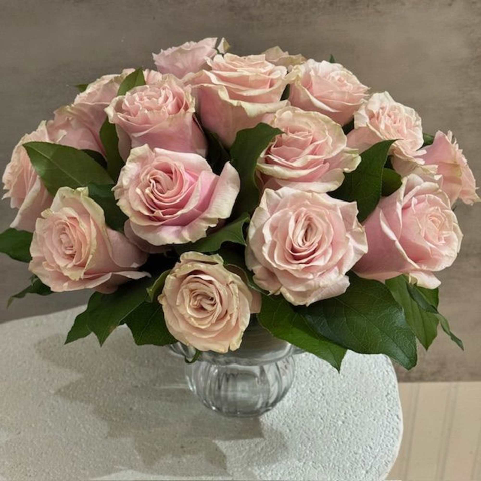 18 soft pink roses designed with greenery in glass pedestal vase measuring