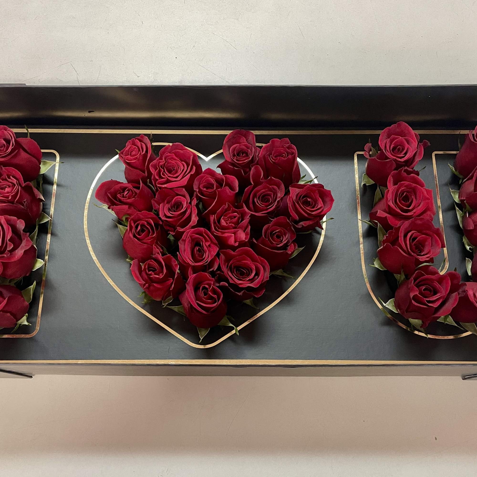 A beautiful display of red roses tucked into a black box spelling