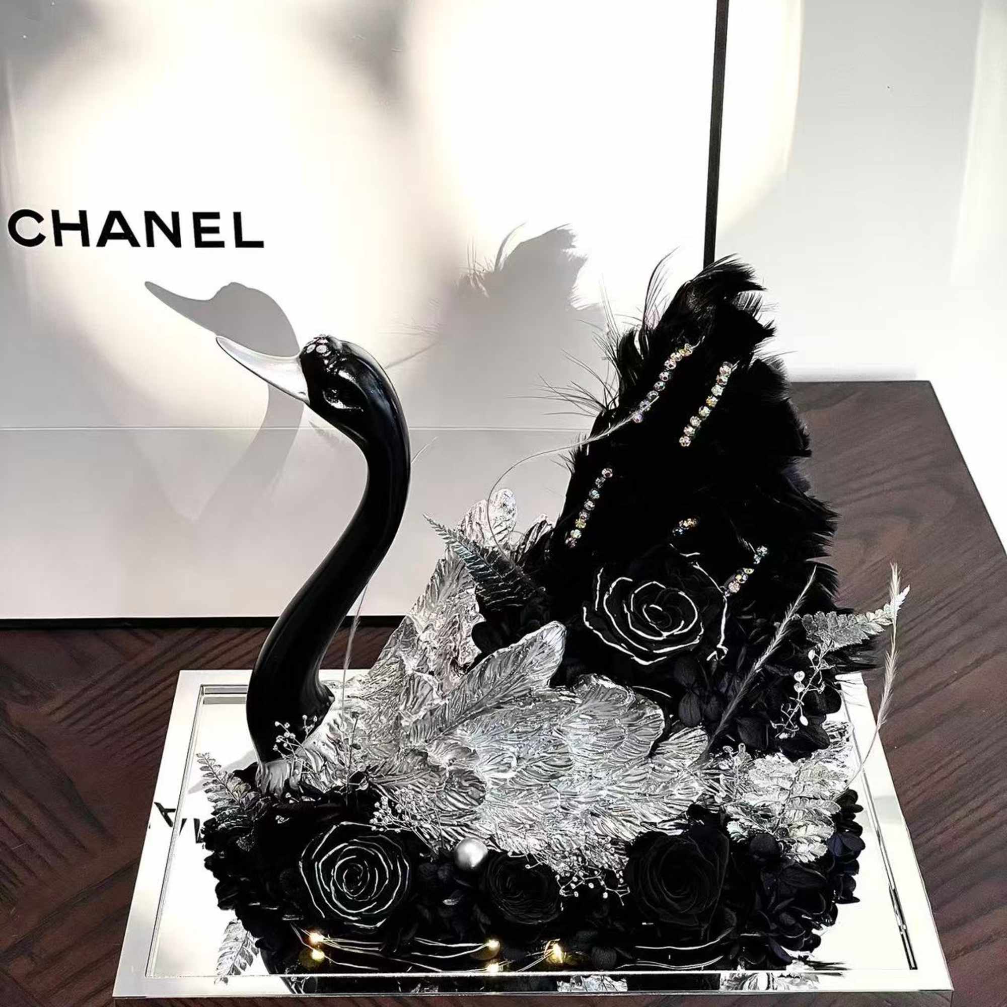 This striking preserved flower arrangement features an elegant black swan sculpture, surrounded