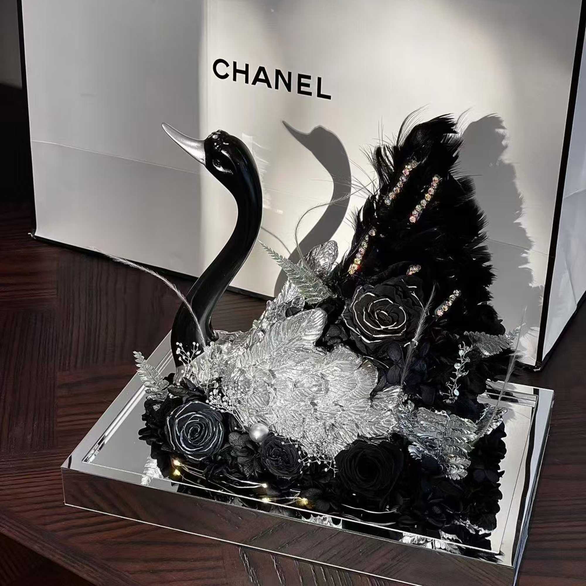 This striking preserved flower arrangement features an elegant black swan sculpture, surrounded