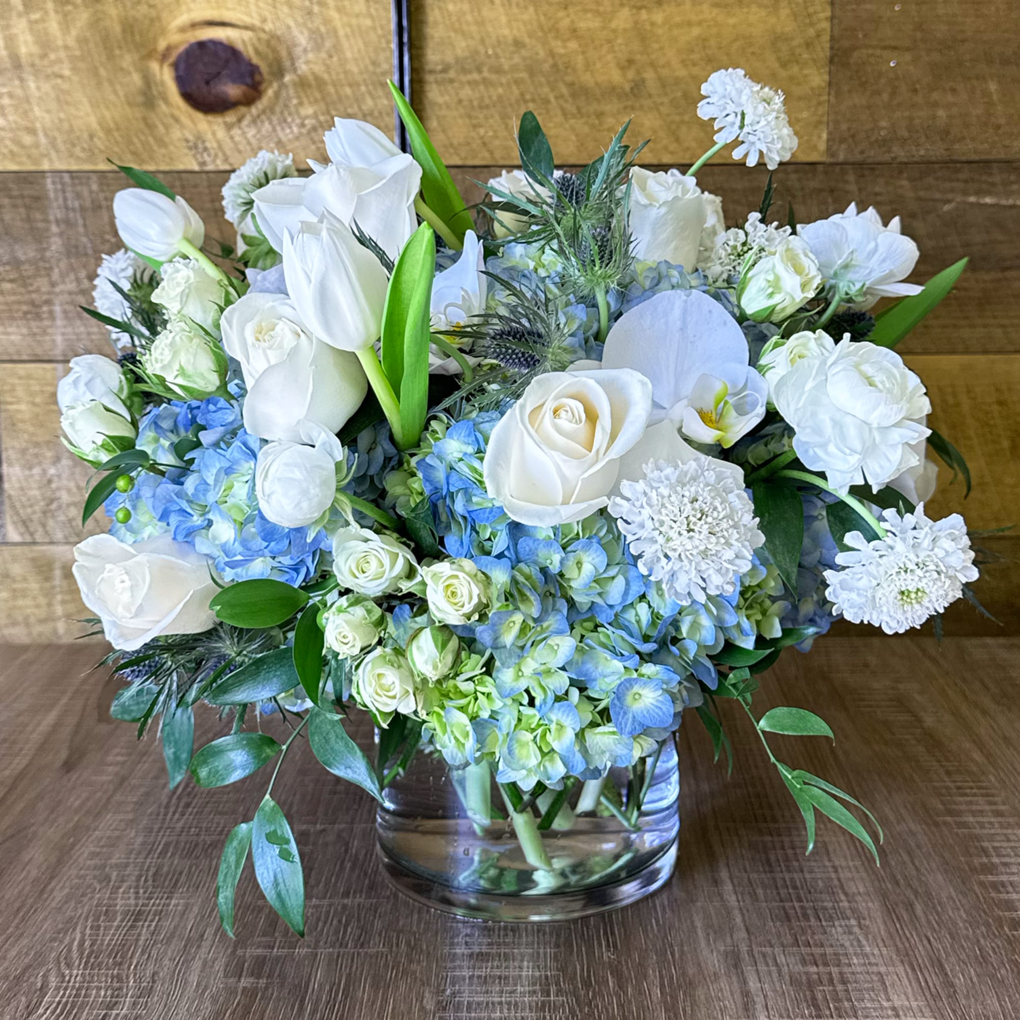 Beautiful round arrangement with a mixture of roses, blue hydrangeas, spray roses