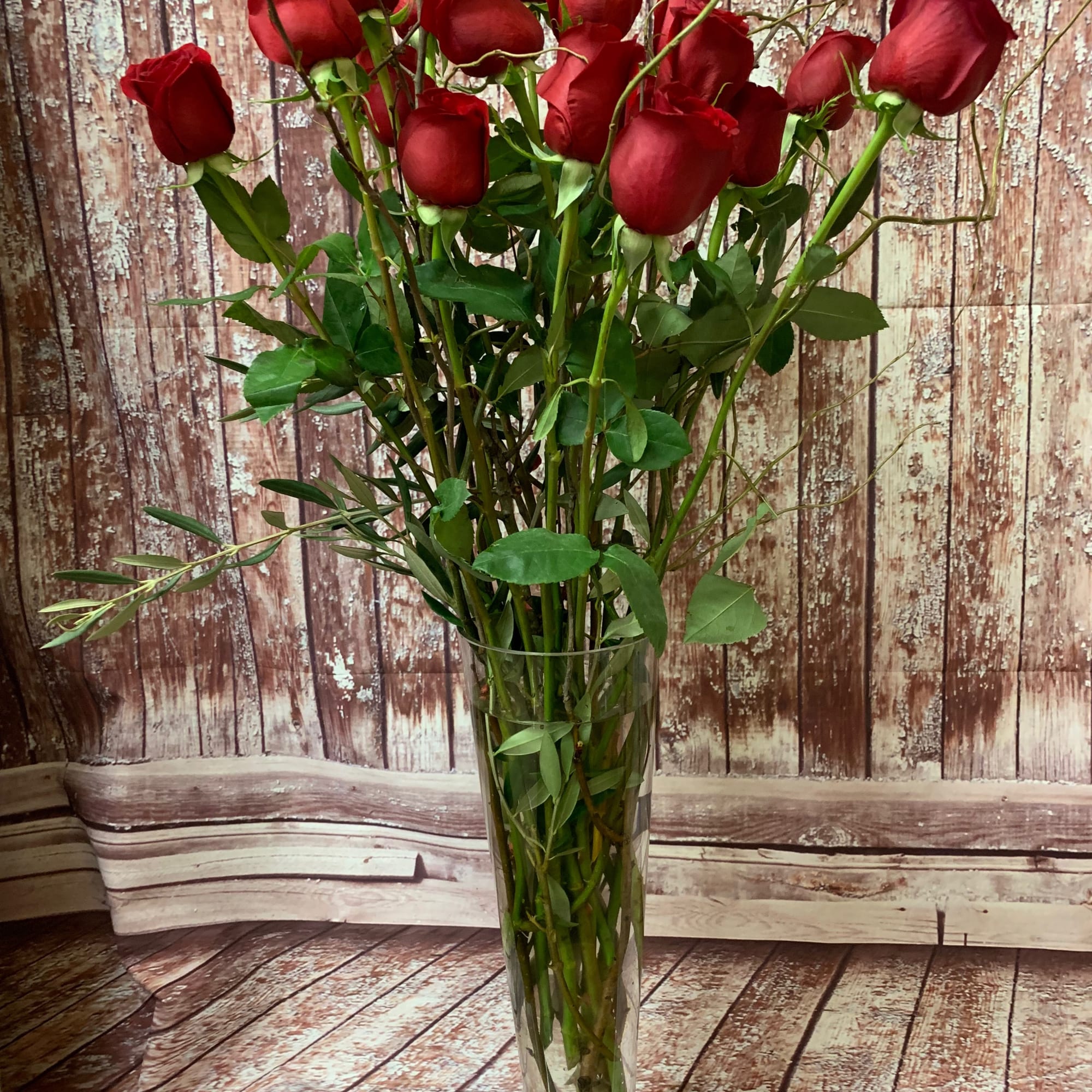 Eighteen long-stemmed red roses, presented in a clear glass or ceramic vase