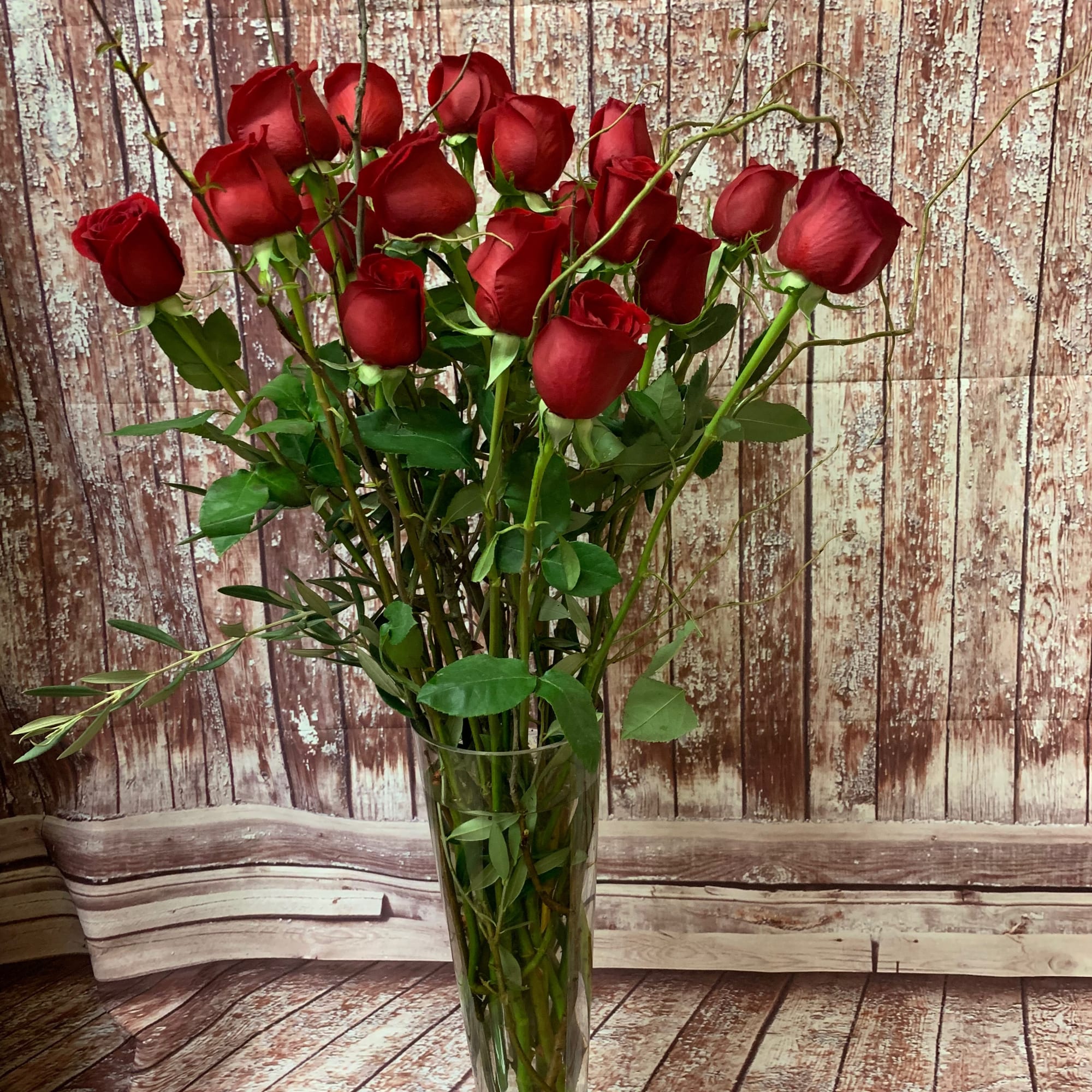 Eighteen long-stemmed red roses, presented in a clear glass or ceramic vase