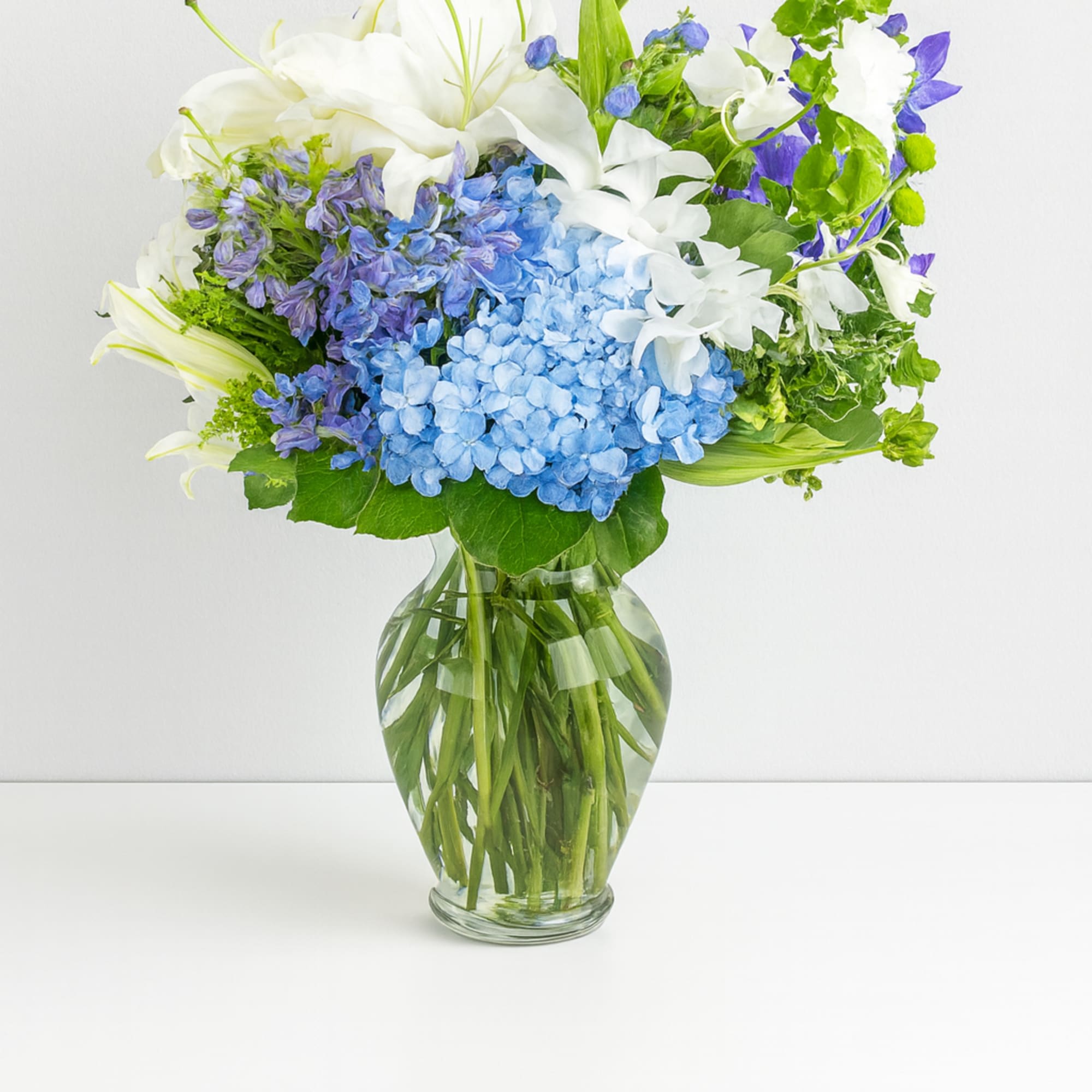This arrangement contains delphinium, bells of ireland, asiatic lilies, hydrangea, blue iris