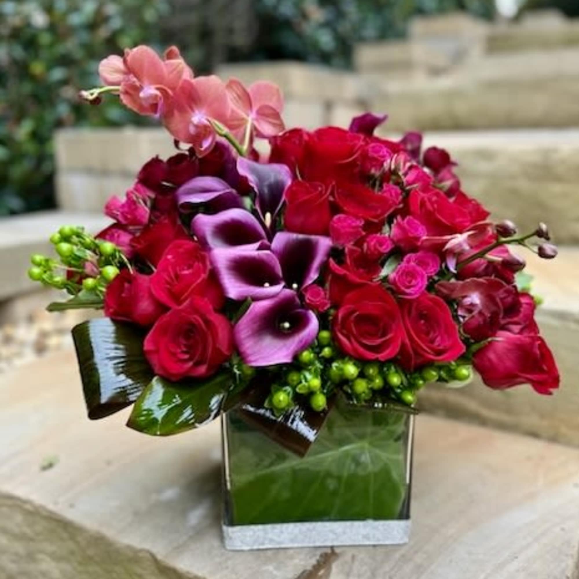 A deep colored modern arrangement with beautiful orchids, calla lilies and a
