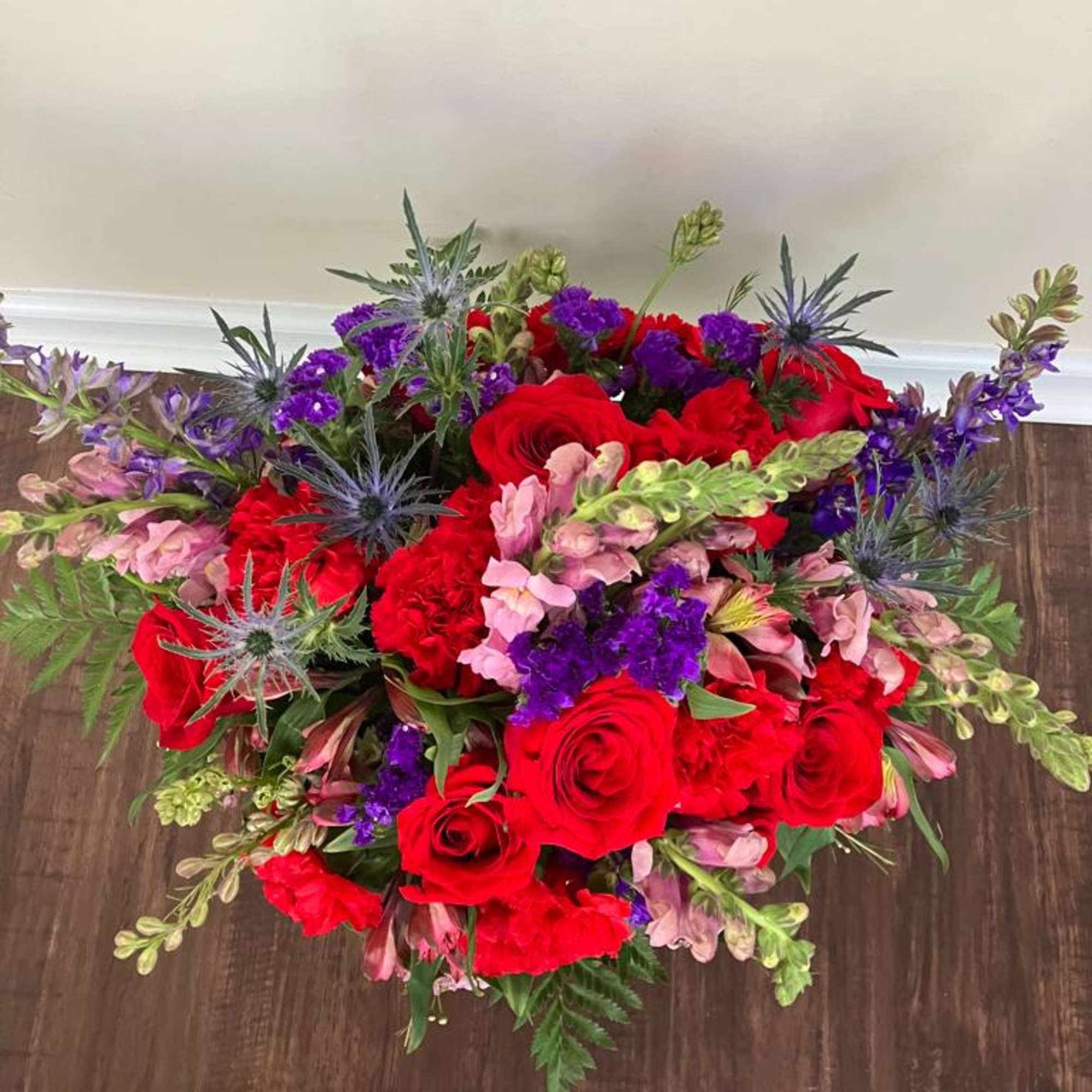 Fresh flower arrangement along fine foliage.

Bloom Details: Snaps/Stock, Roses, Thiesel, Carnations, Statice