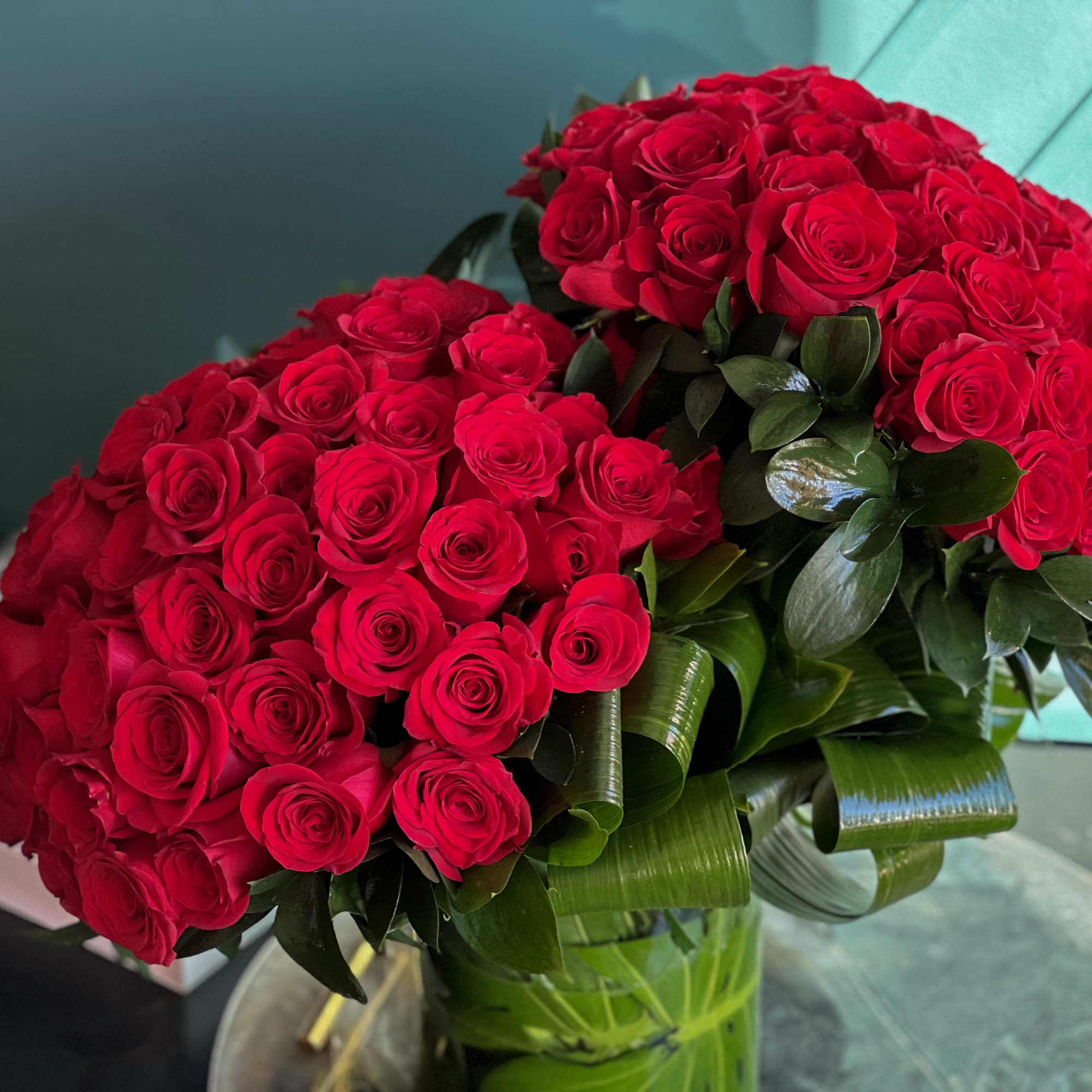 100 premium red roses in a clear vase with greenery accent 