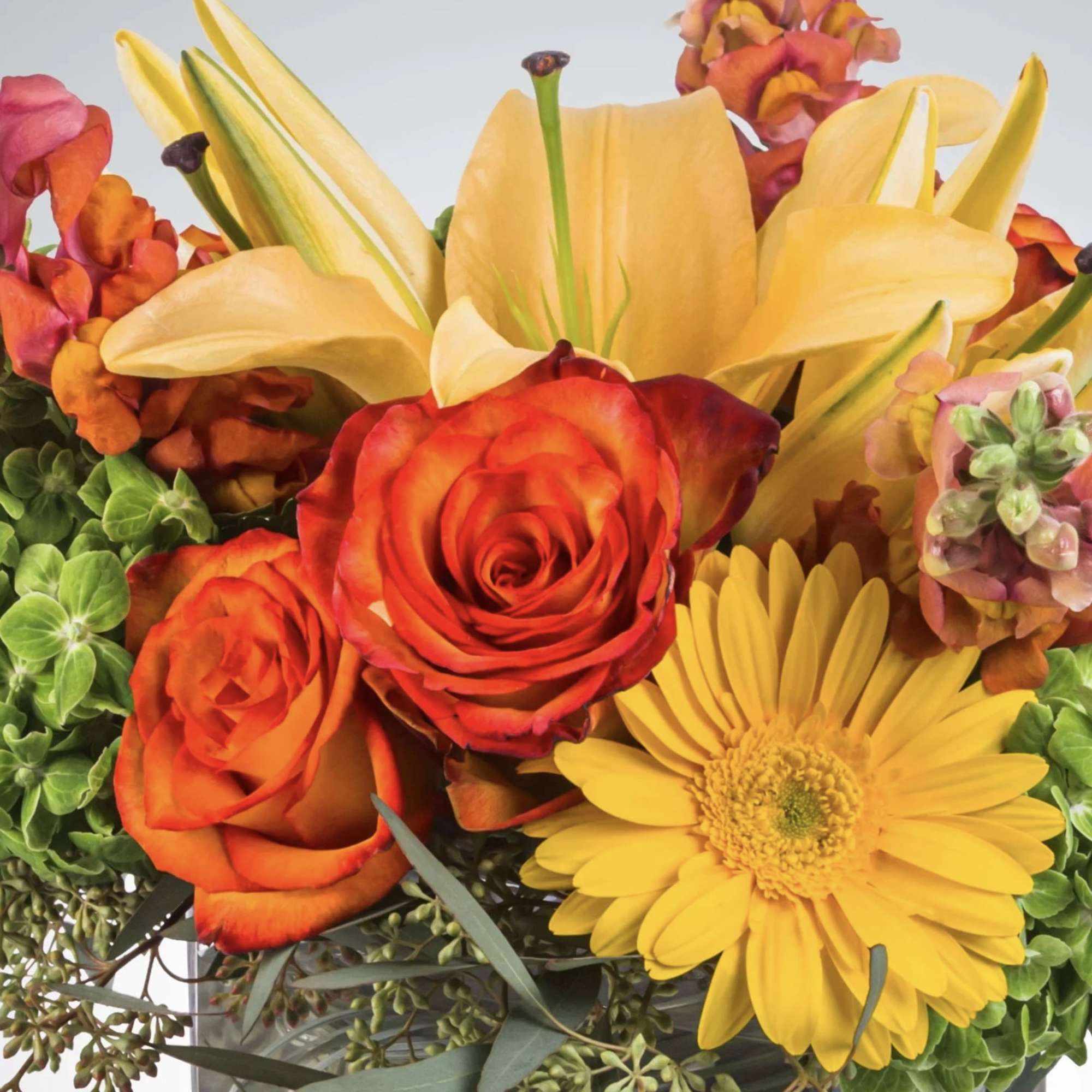 This bright yellow, green, and orange arrangement includes roses, daisies, and lilies