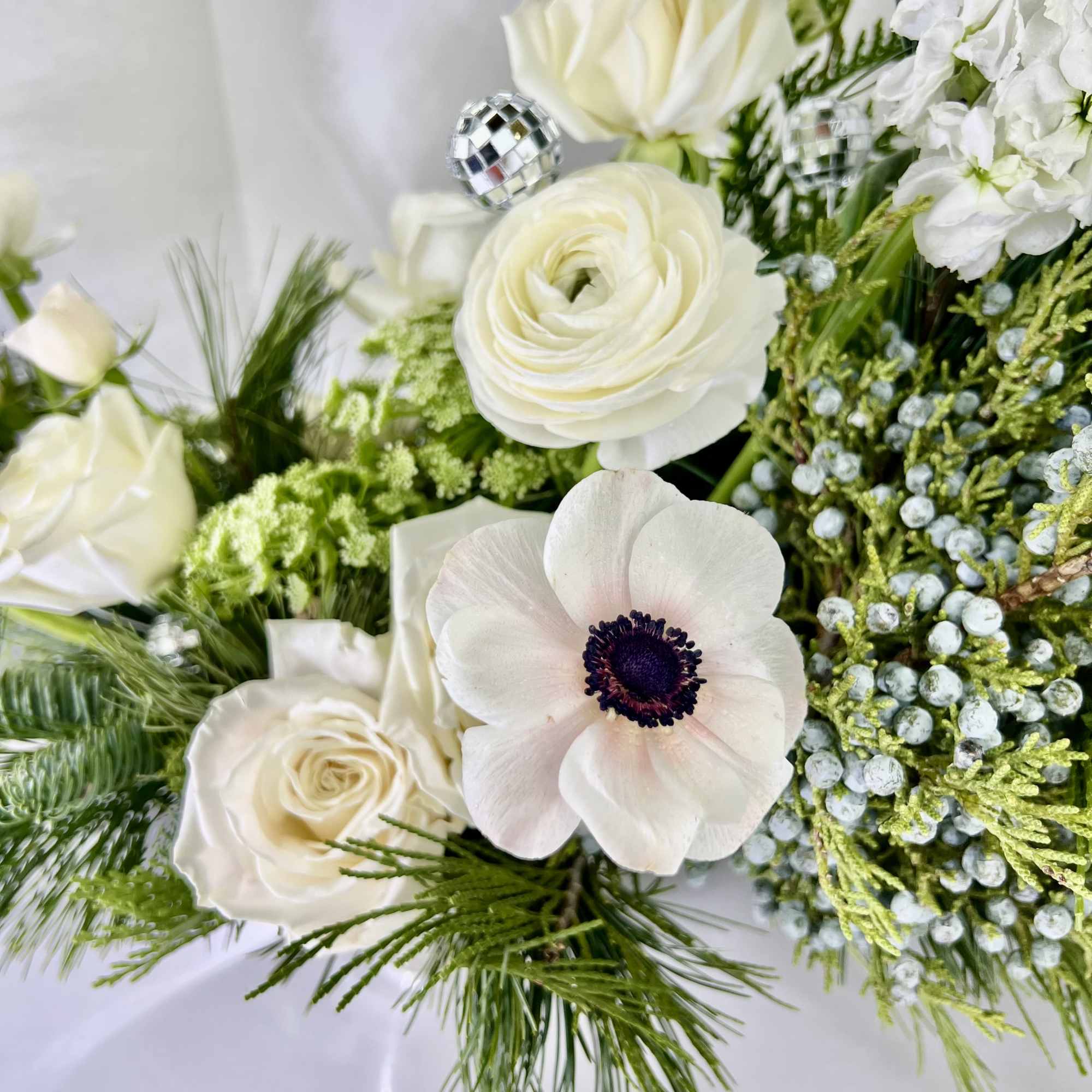 Stunning mix of white blossoms nestled into long lasting winter evergreens. 