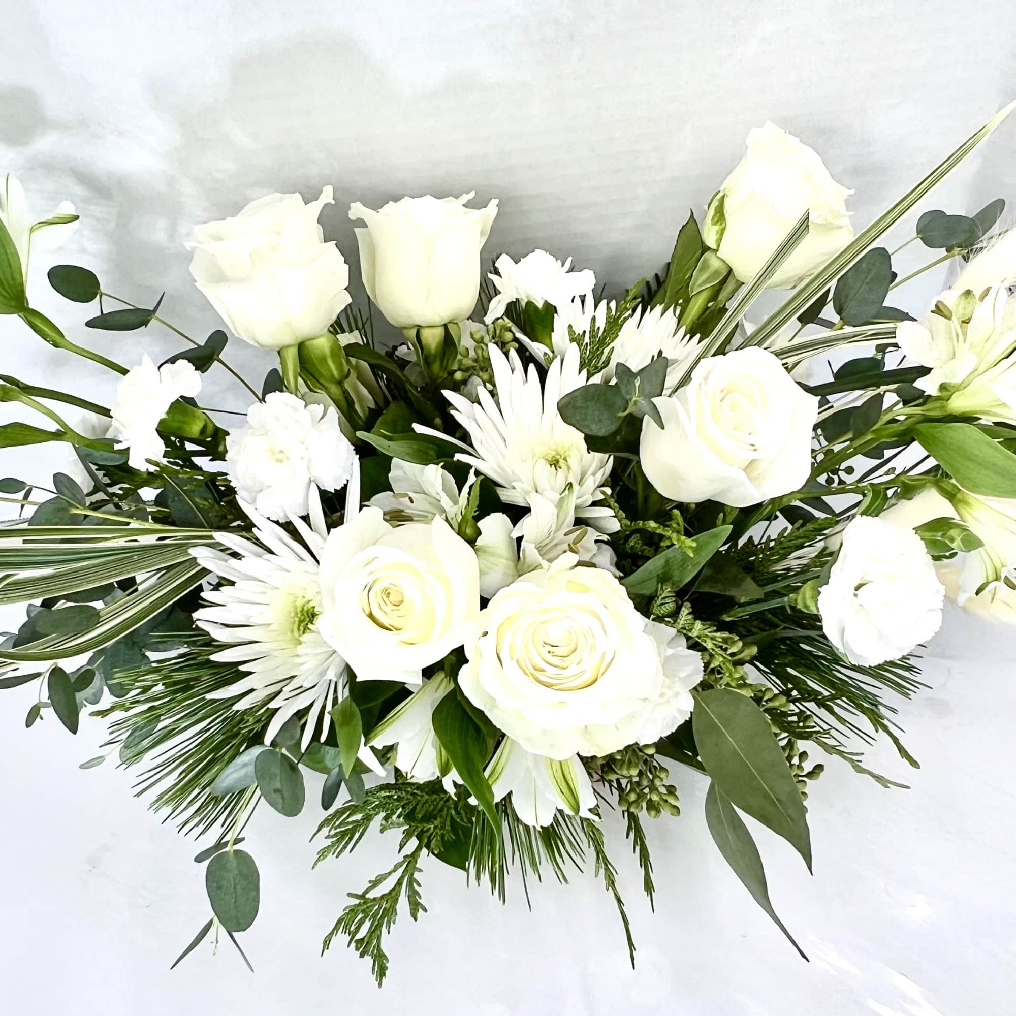 Stunning mix of white blossoms nestled into long lasting winter evergreens. 