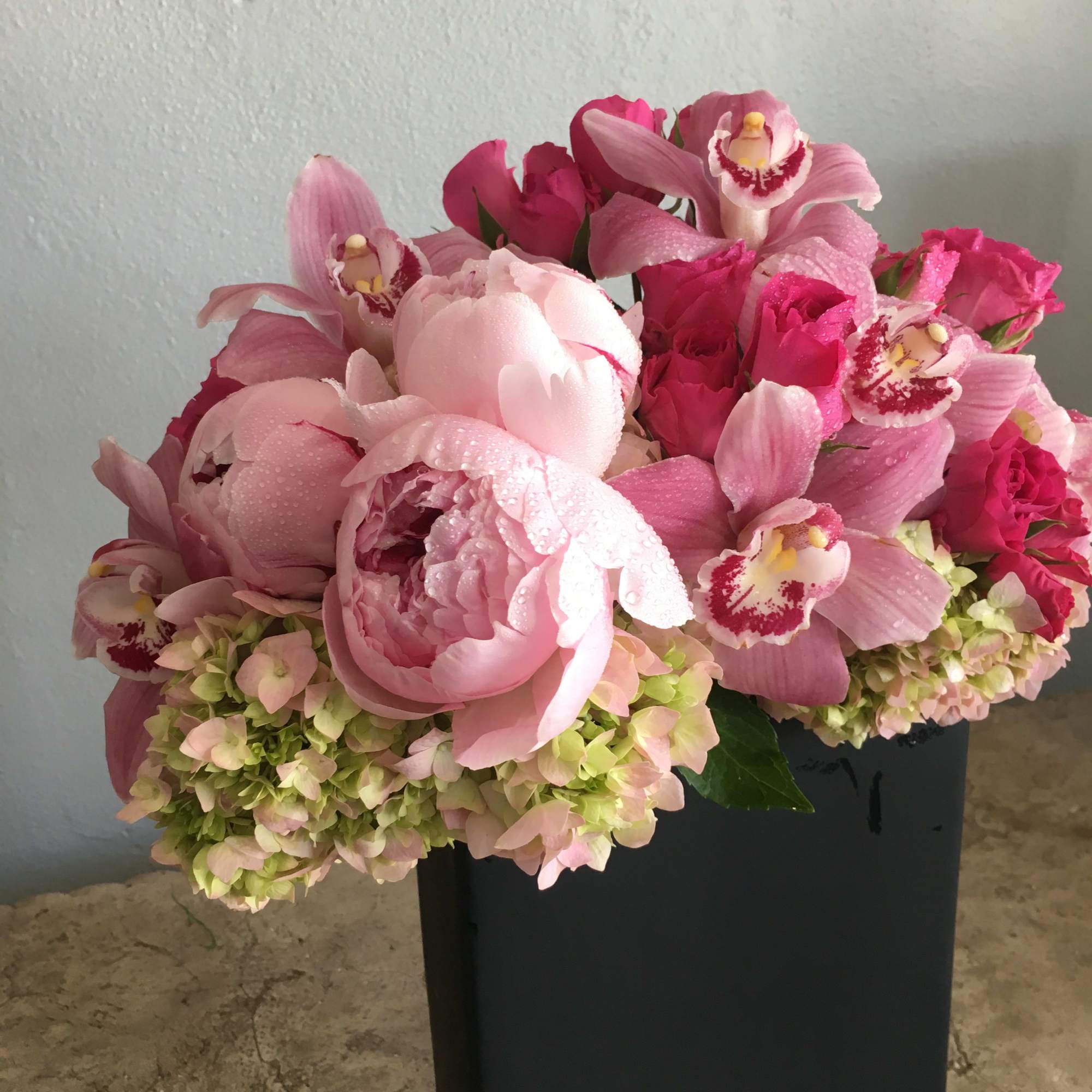 Lush peonies, cymbidium orchids, hydrangeas flowing over the edges of a black