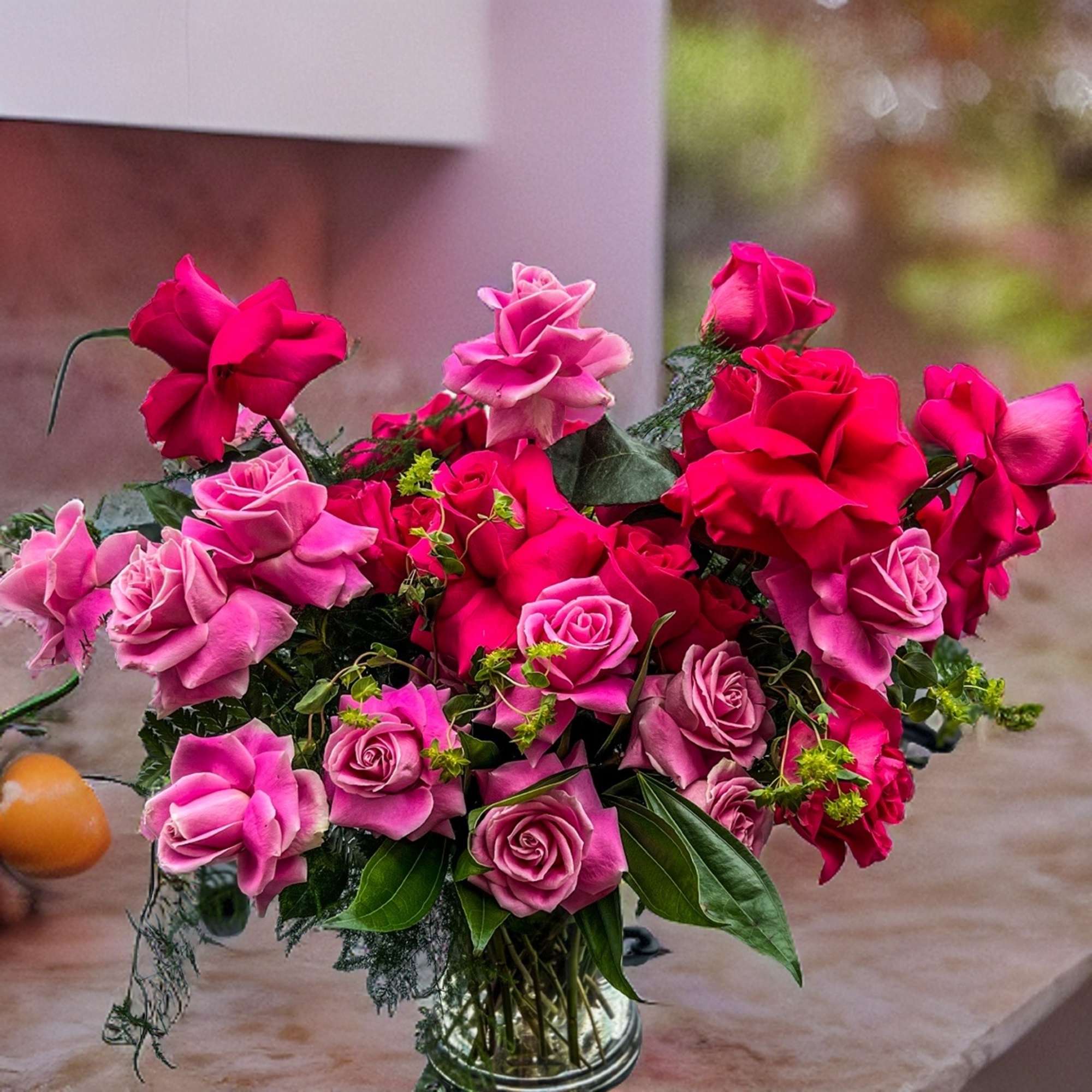 Different shades Premium Roses designed with greenery in clear vase.