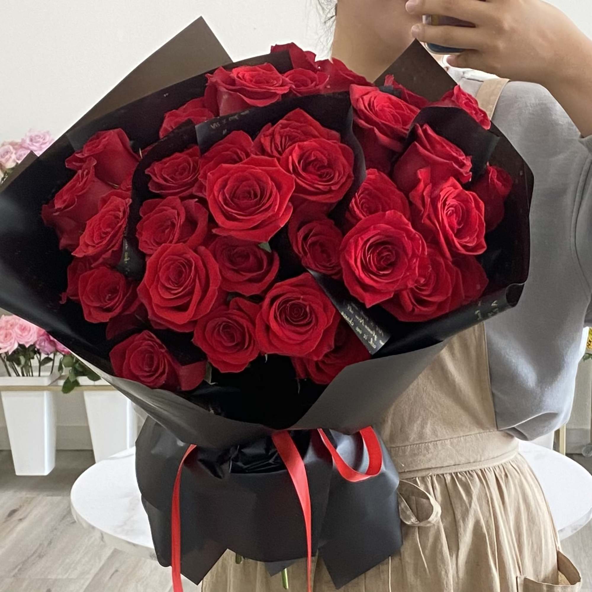 A front-facing bouquet of roses with layered paper accents, wrapped in black