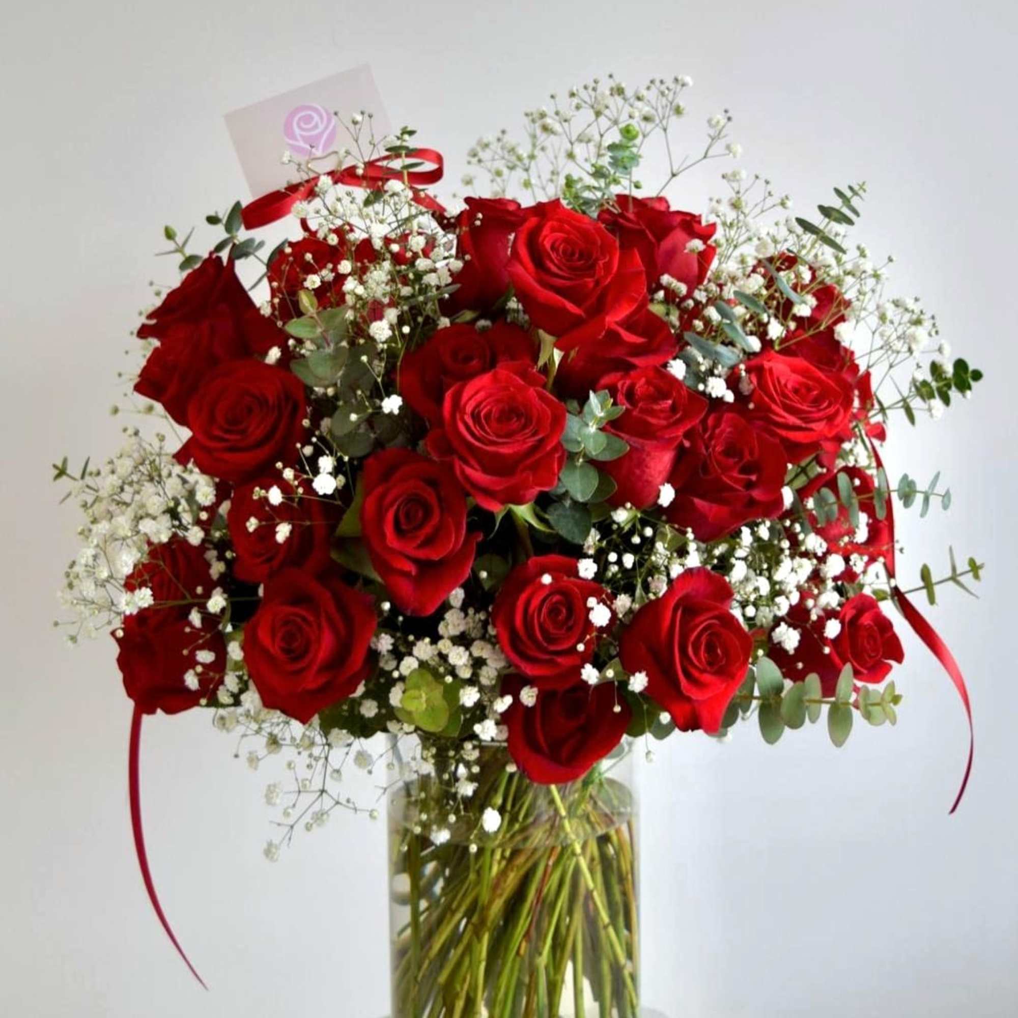 A medium cylinder glass vase with red roses, baby's breath, and eucalyptus.