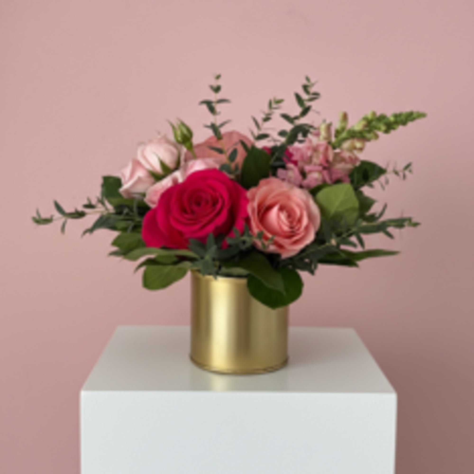 A gold pot filled with shades of pink flowers and foliage. Something