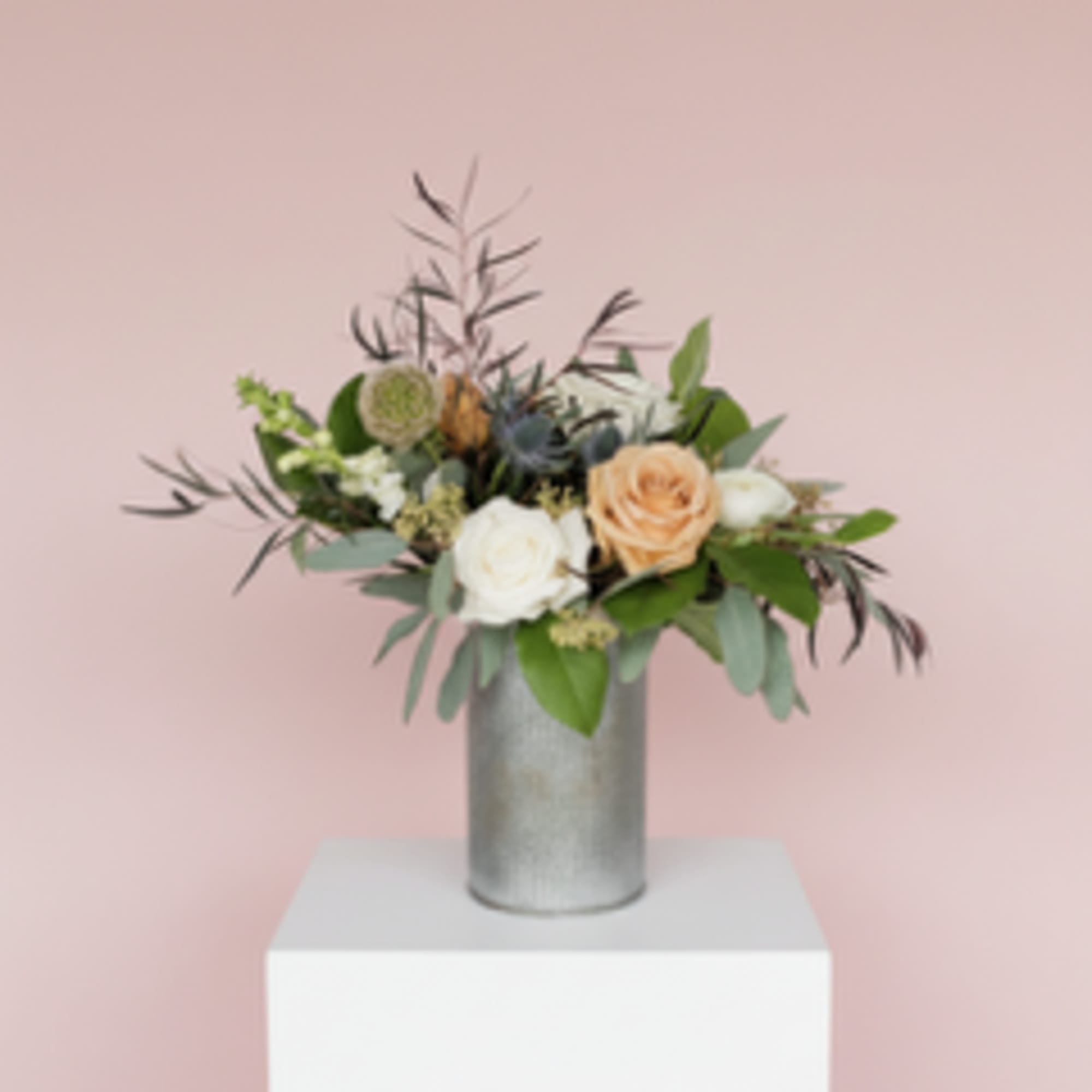 Woodsy floral arrangement including seasonal blooms and foliage in a tin vase.